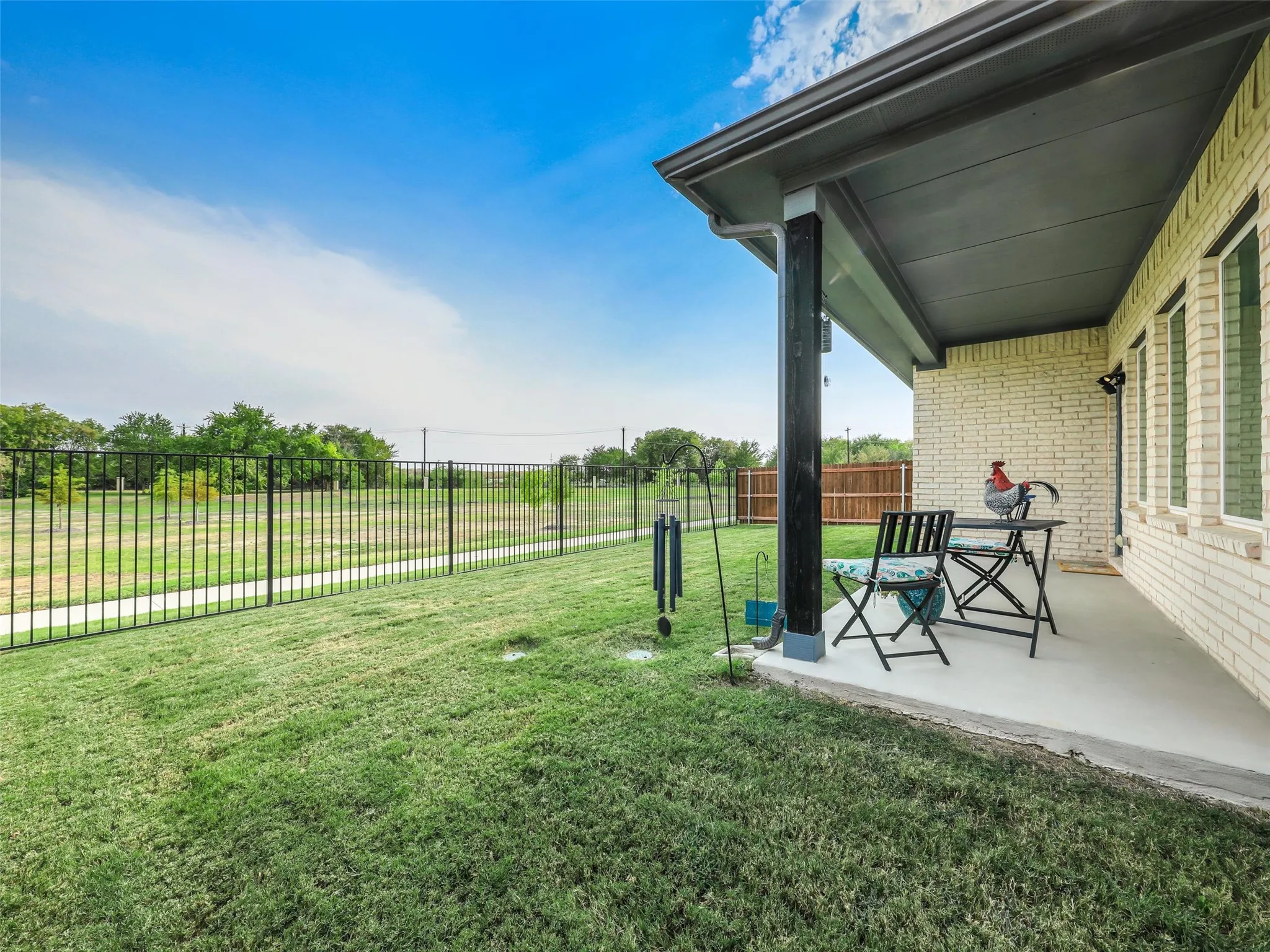 Expansive lawn area with black metal fencing, a covered concrete patio, and a light brick exterior