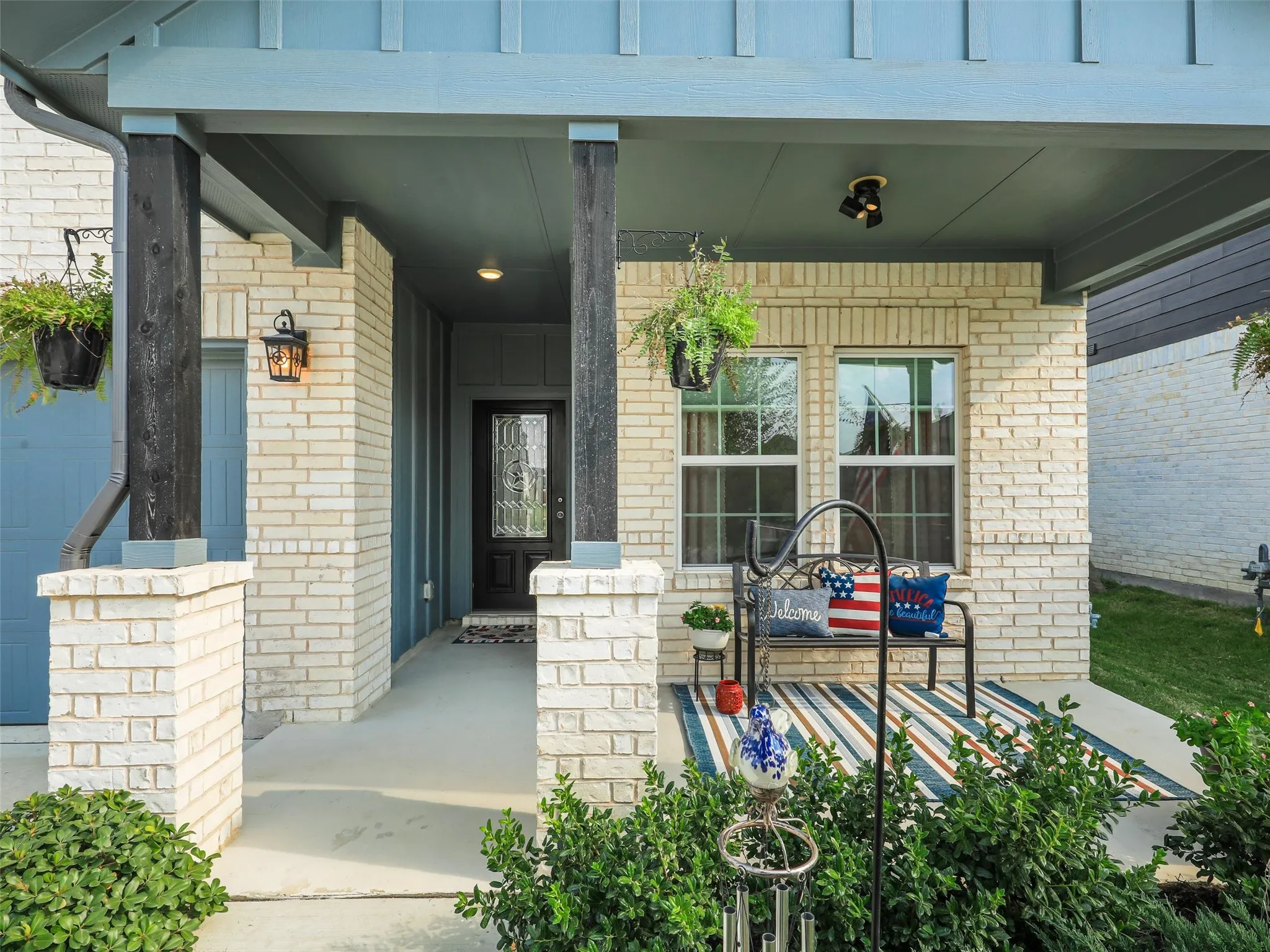 Covered front porch with cream brick exterior, black-framed multi-pane windows