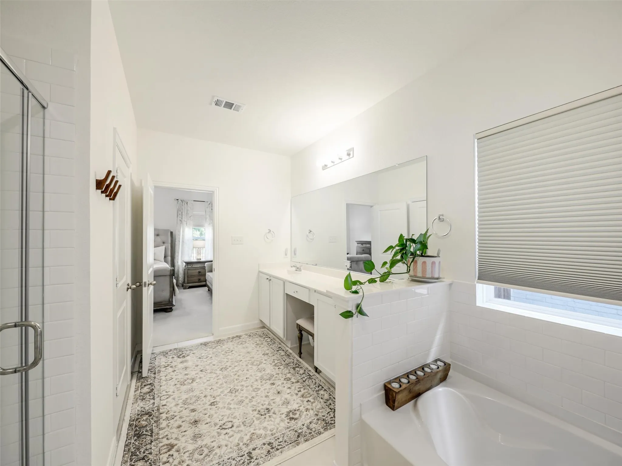 White subway tile shower with glass enclosure, dual vanity with undermount sinks, white countertop, and built-in soaking tub