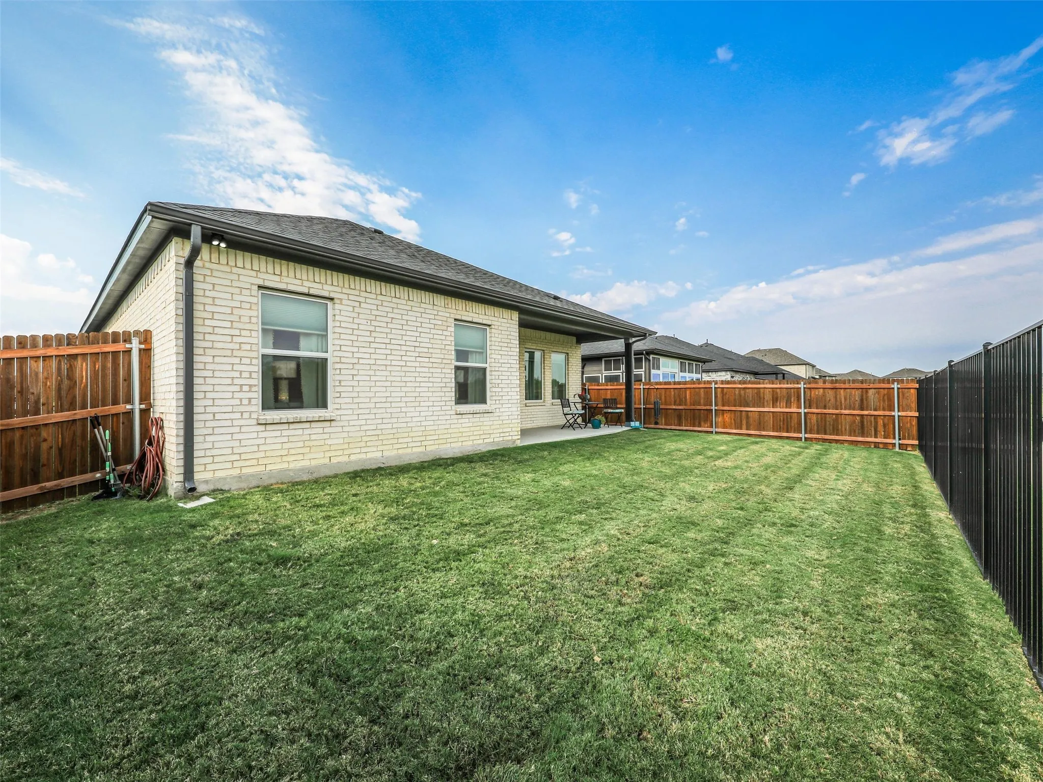 Expansive backyard featuring a manicured lawn, a covered patio, and a light brick exterior with multiple windows
