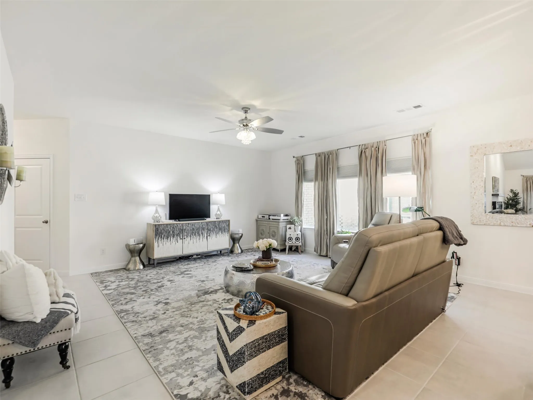 Recessed lighting, ceiling fan, expansive windows with drapes, and light-toned tile flooring