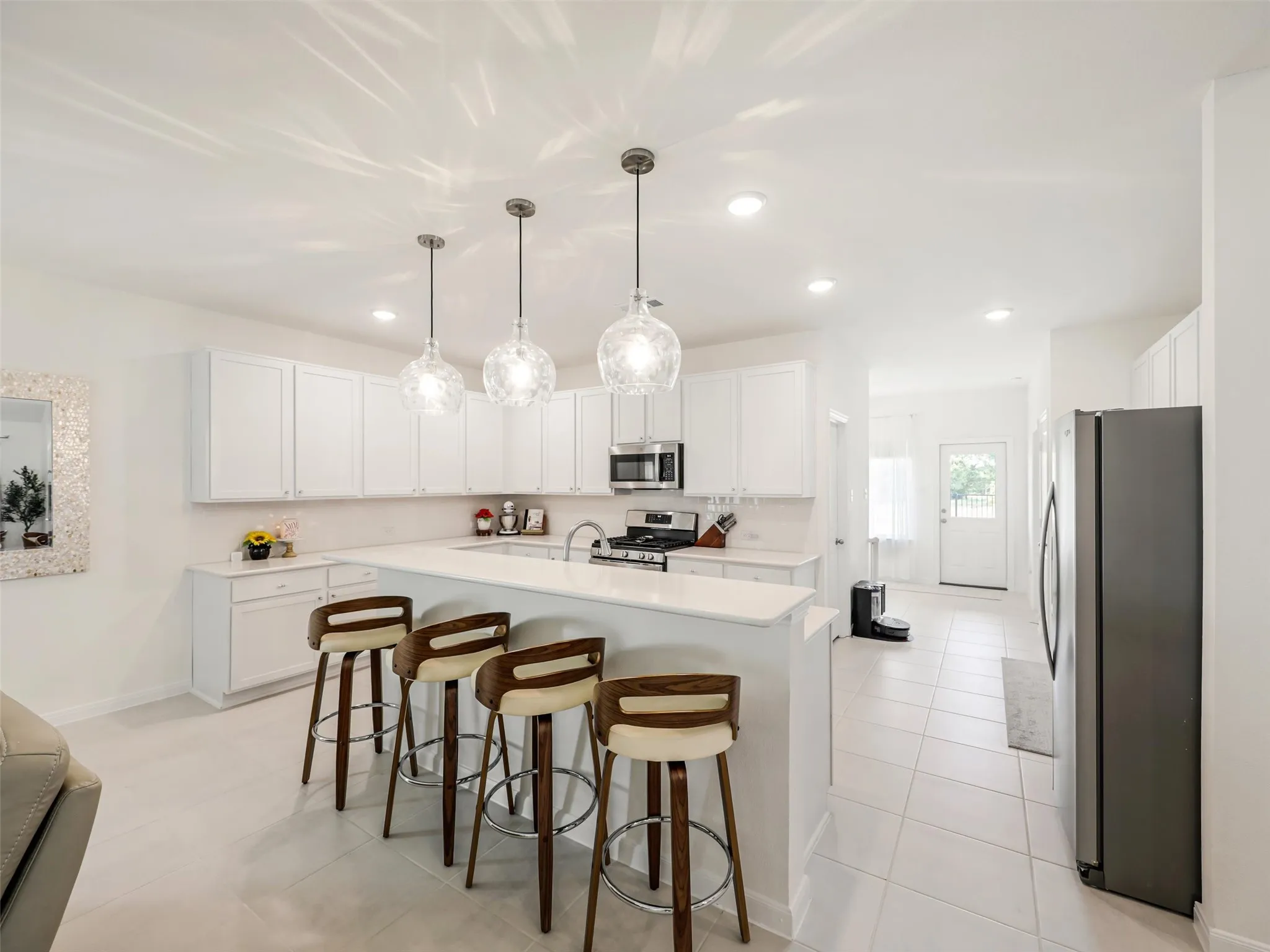 White cabinetry, stainless steel appliances, solid surface countertops, tile flooring, and pendant lighting