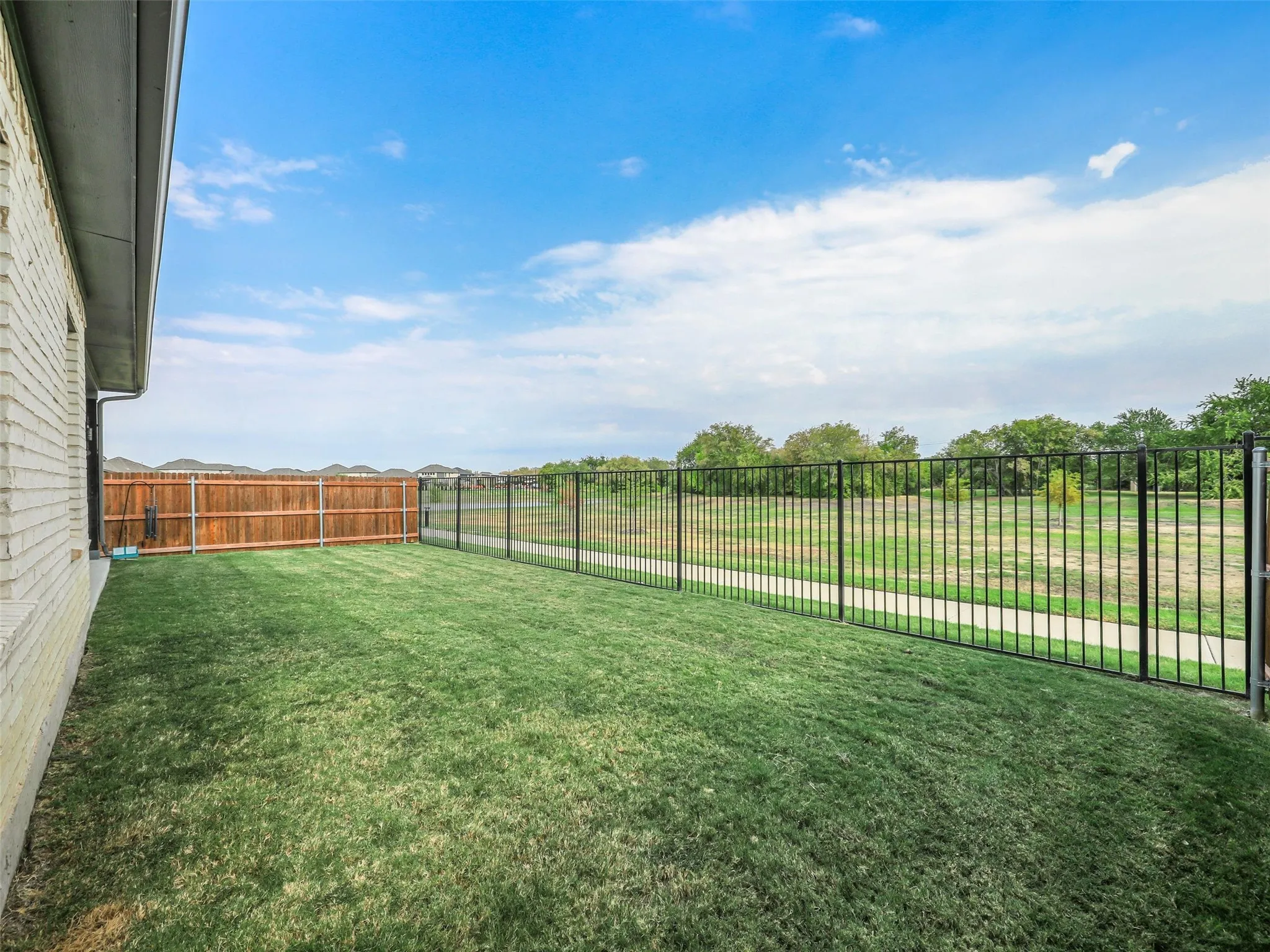 Expansive grassy yard with a privacy fence and black metal fencing
