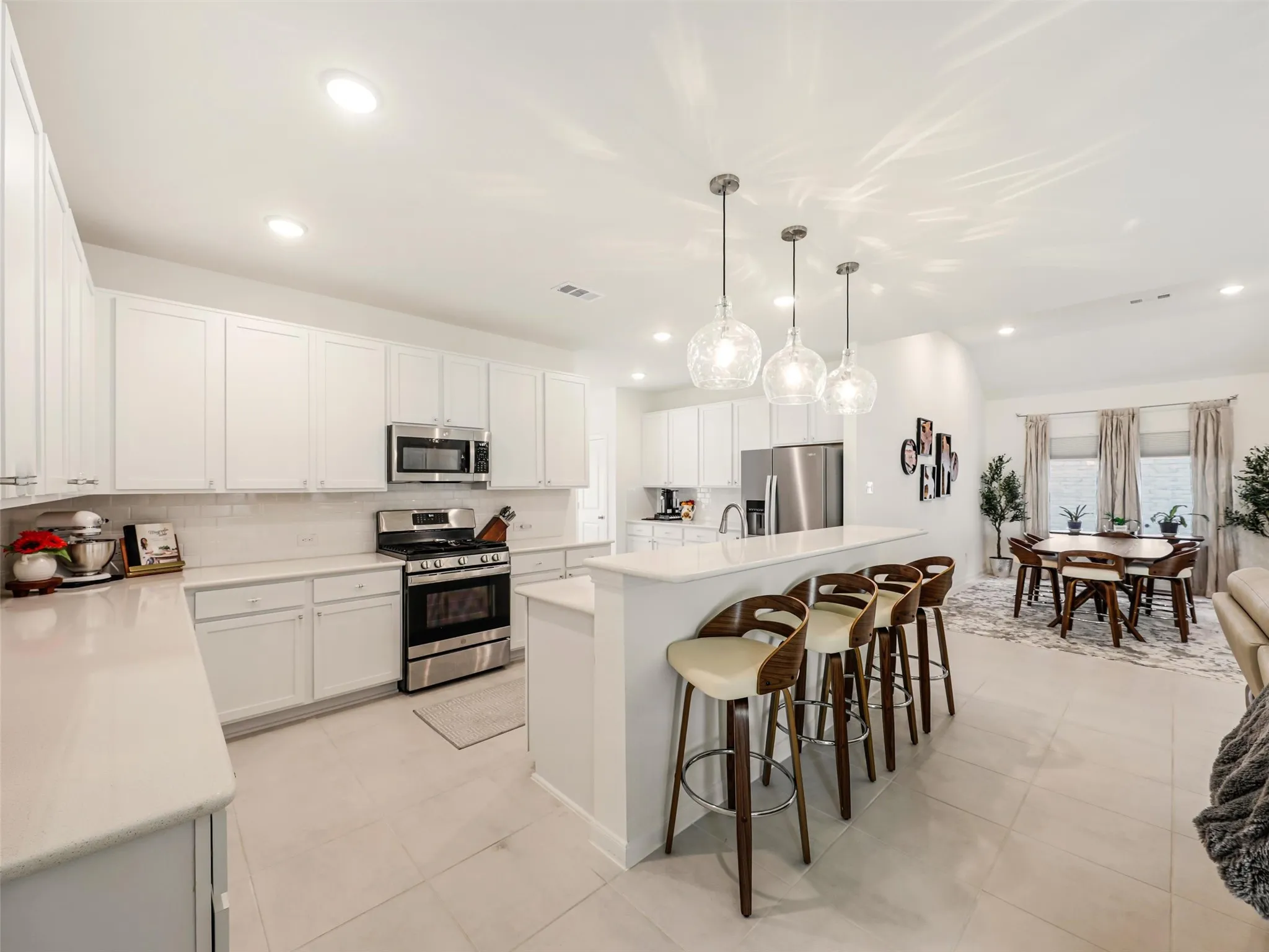 White flat-panel cabinetry, stainless steel appliances, light-toned countertops, tile flooring, and recessed lighting