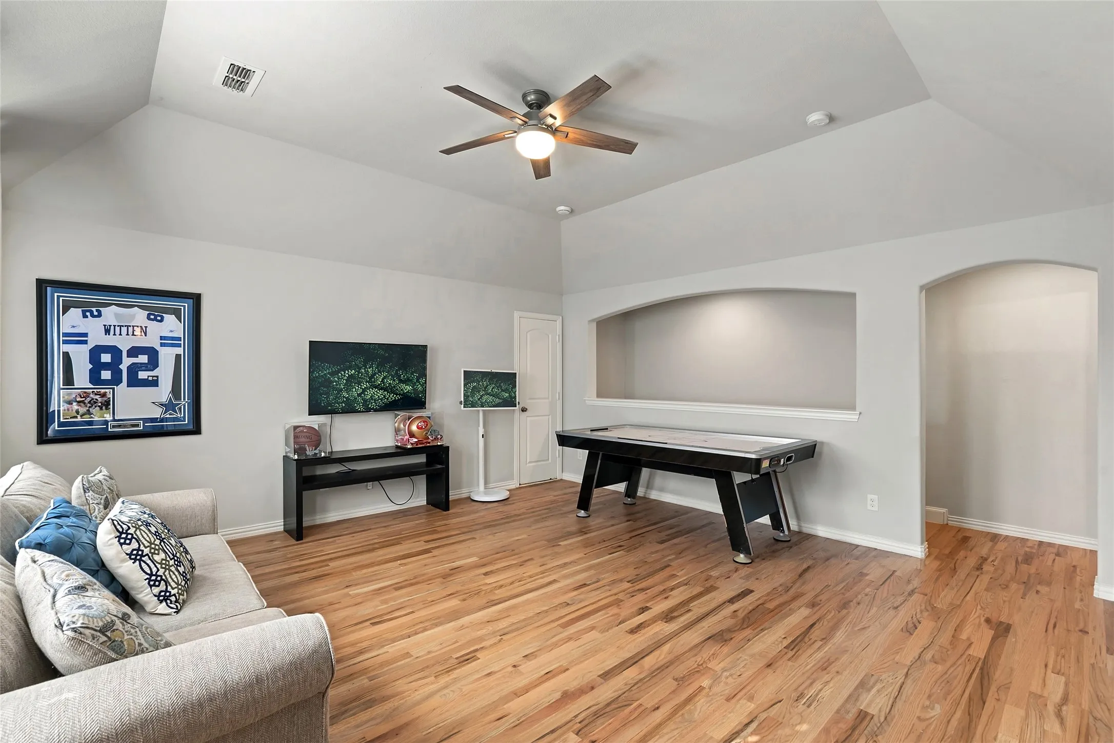 Vaulted ceiling with a ceiling fan, recessed wall niche, arched doorway, and wood-finish flooring