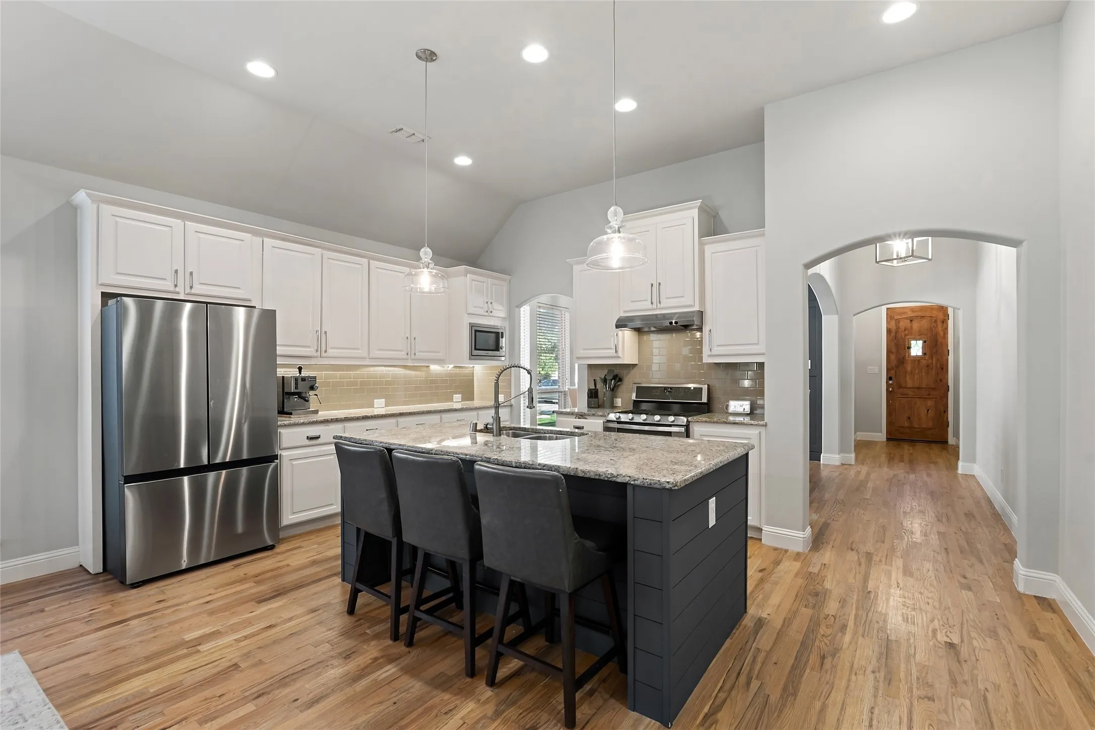 Kitchen featuring wood-finish flooring, white cabinetry, a central island with countertop seating, stainless steel appliances, and recessed lighting
