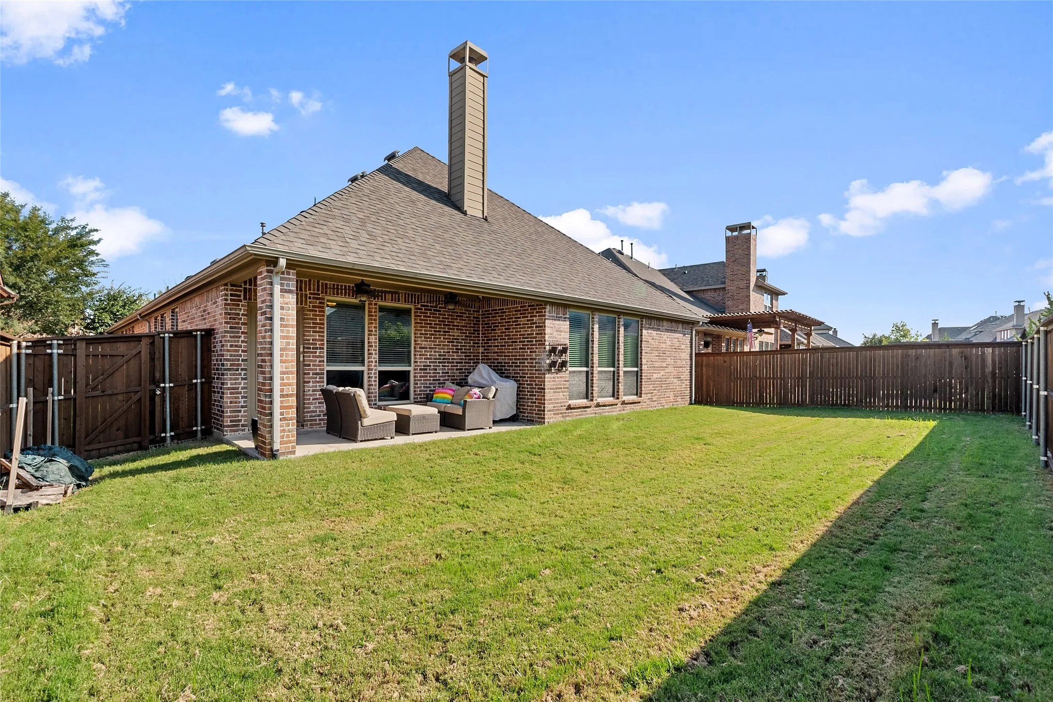 Expansive backyard featuring a manicured lawn, brick exterior, covered patio, and wood privacy fencing