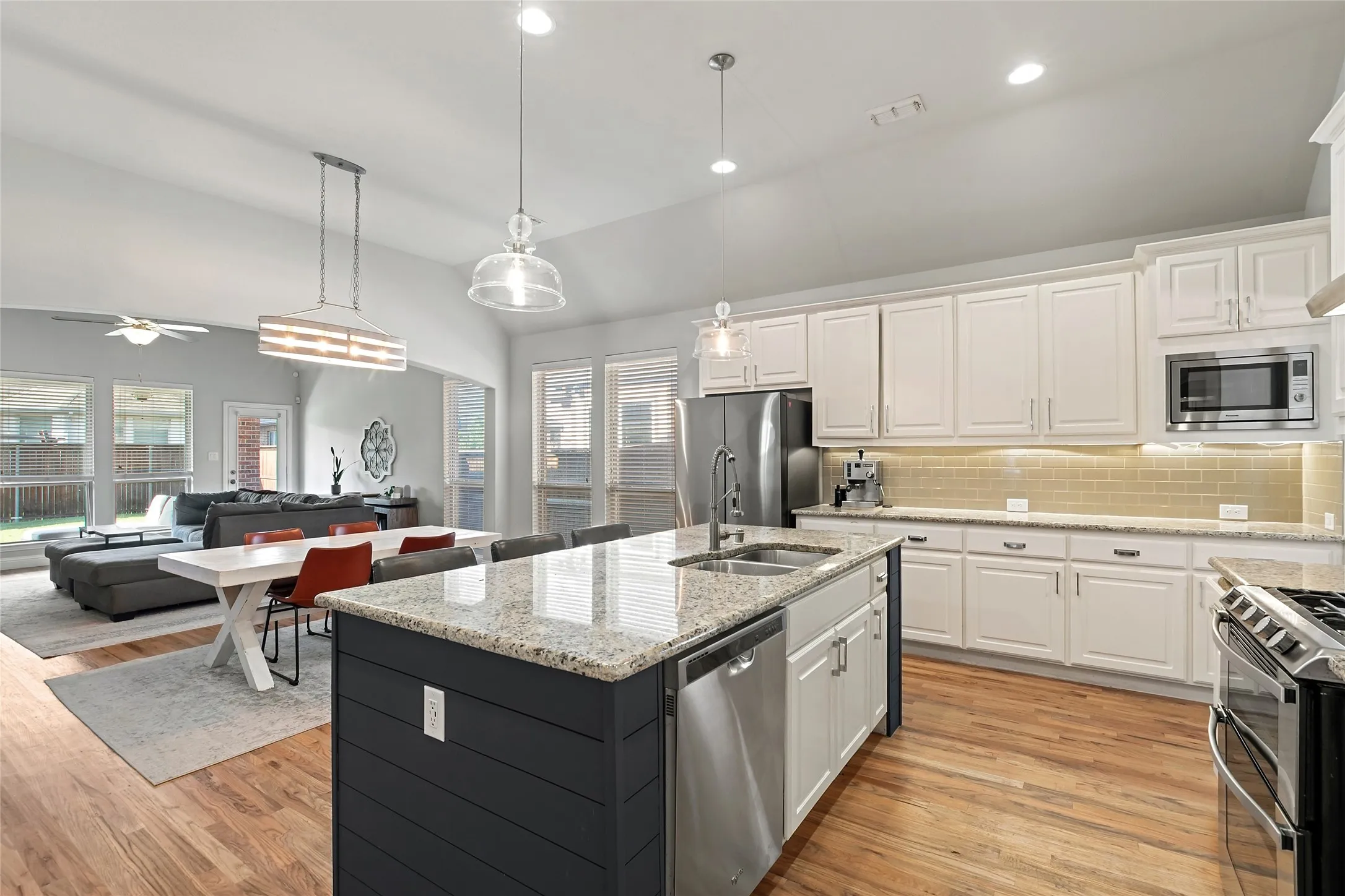 Vaulted ceilings, wood-finish flooring, white cabinetry, granite countertops, and stainless steel appliances