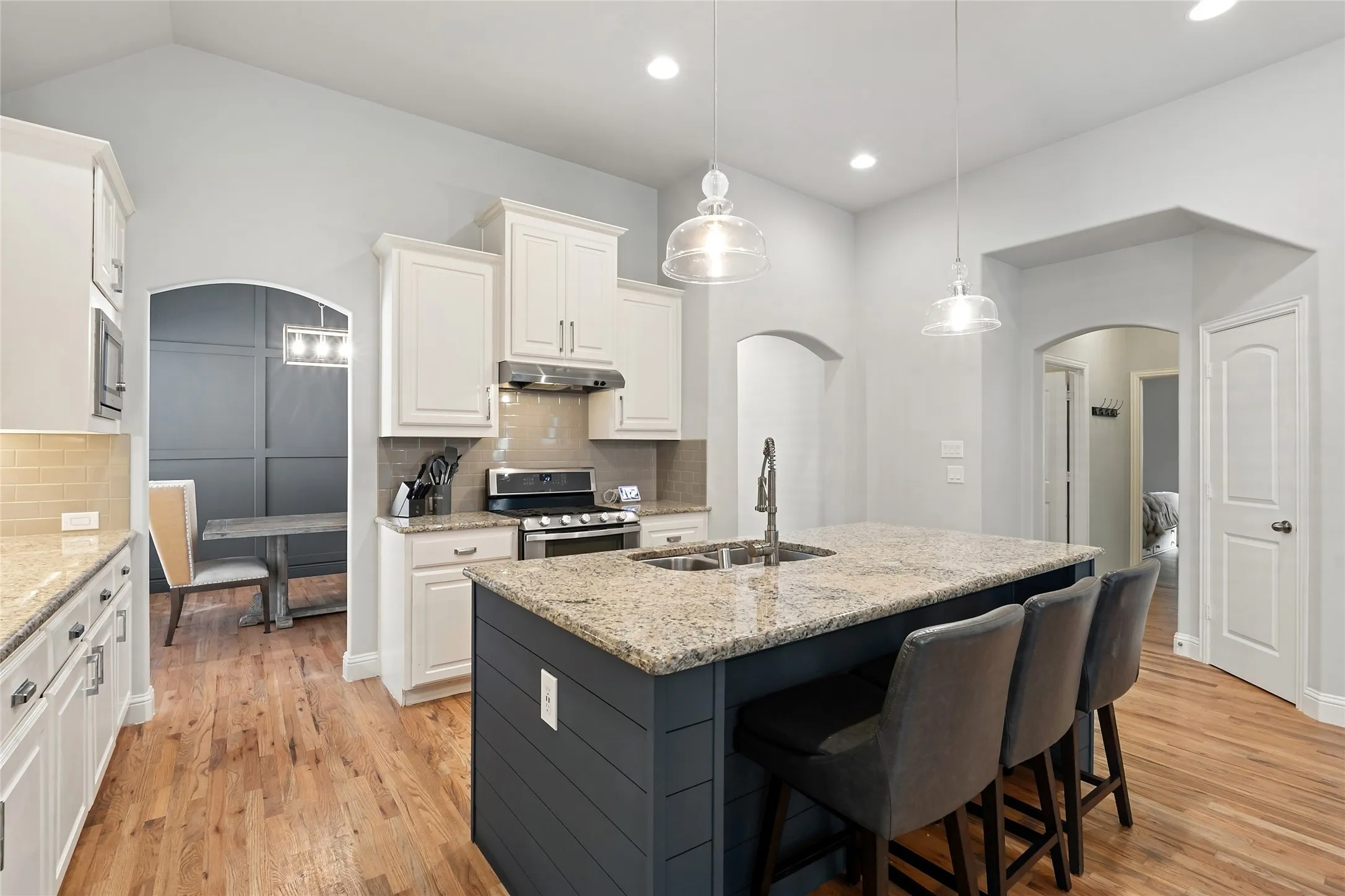 Spacious kitchen featuring an island with stone countertops, stainless steel appliances, a tile backsplash, and light wood-finish flooring