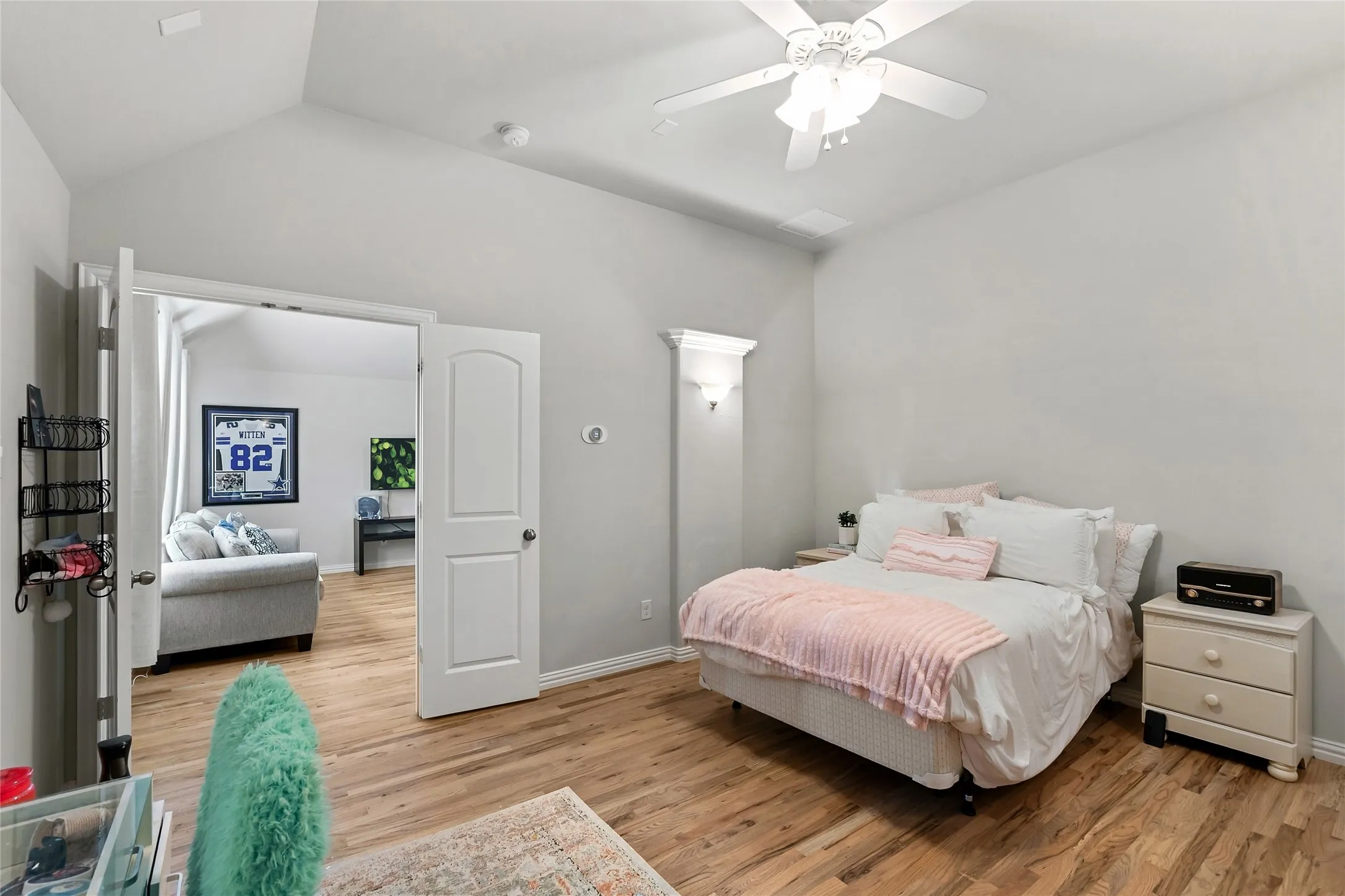 Vaulted ceiling, wood-finish flooring, ceiling fan, wall sconce, and white paneled doors