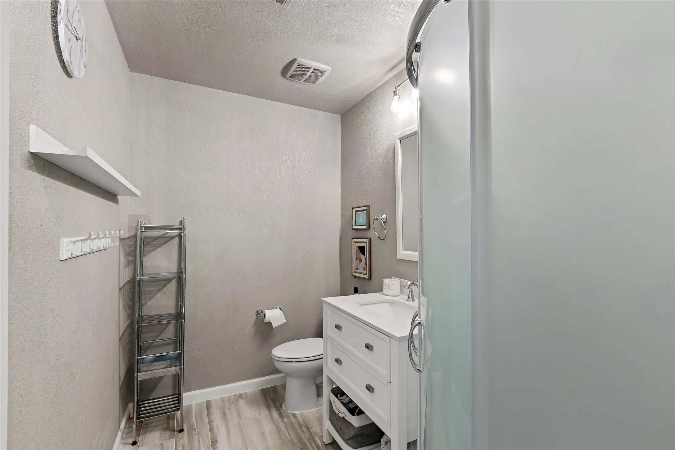 Modern vanity with a white countertop, wood-finish flooring, and a shower enclosure featuring a frosted panel