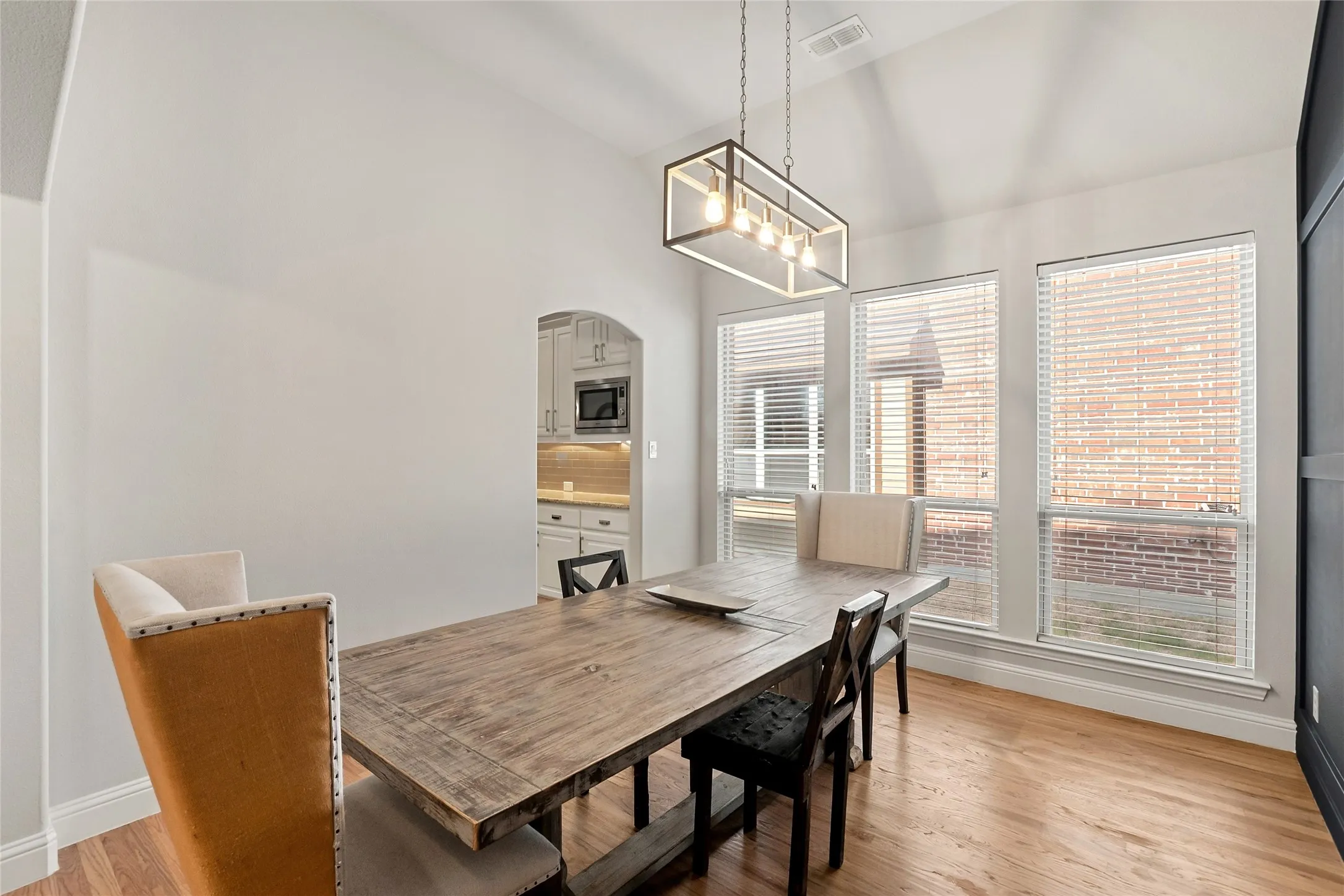 Vaulted ceiling with an architectural light fixture, three windows with blinds, wood-finish flooring, and an arched doorway to the kitchen