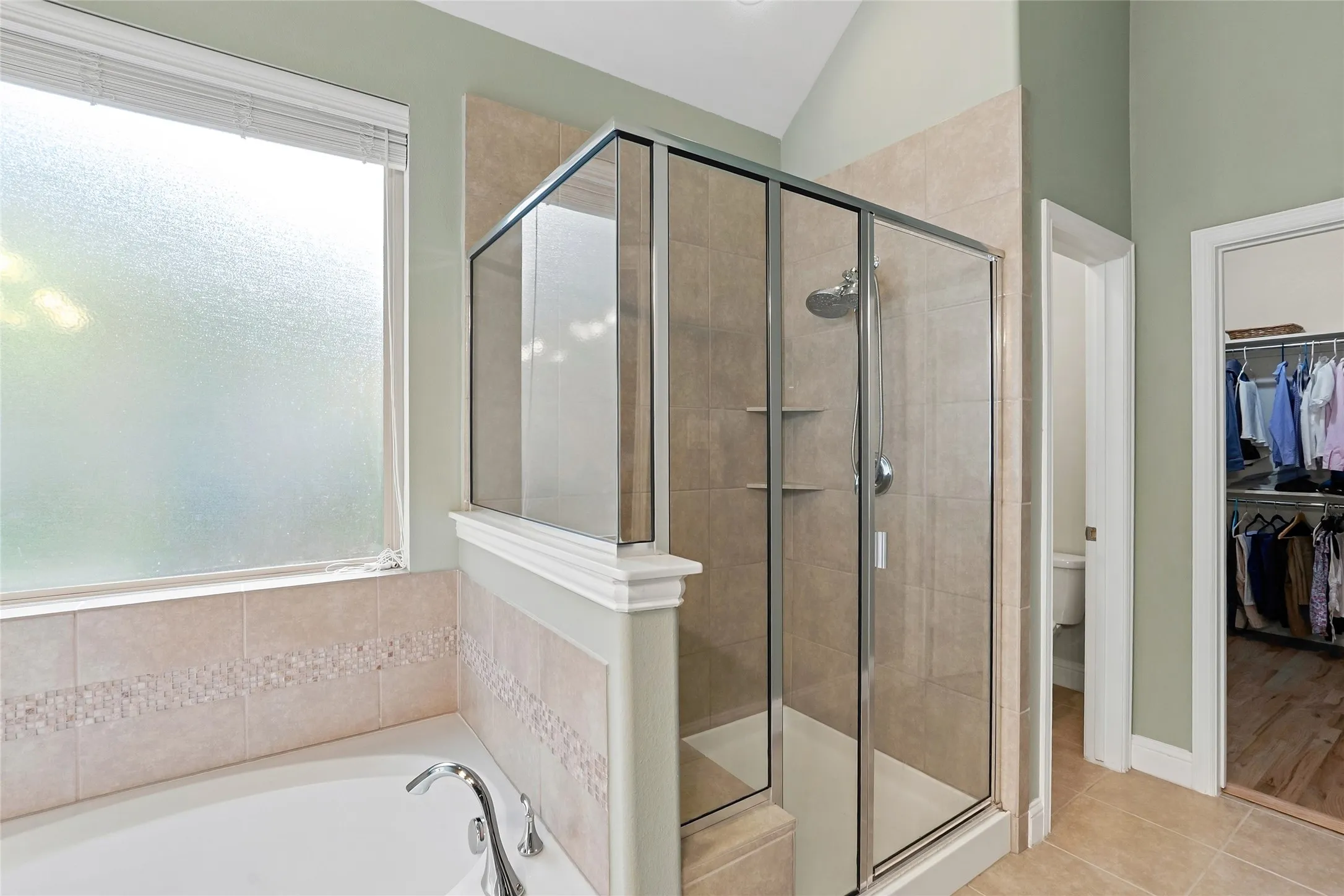 Built-in soaking tub with chrome fixtures, tiled surround with mosaic accent, and an enclosed shower with glass doors and tiled walls