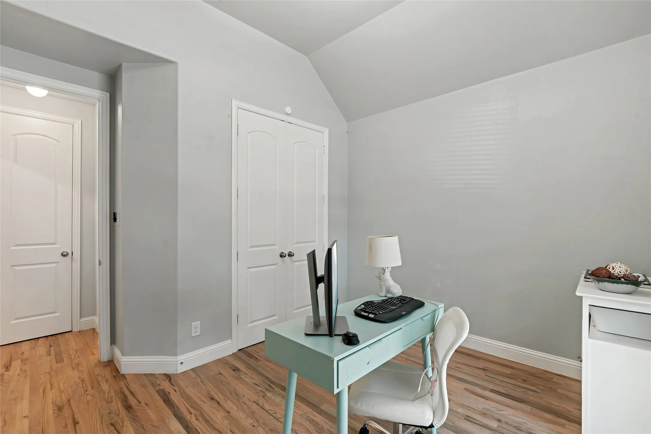 Wood-finish flooring, vaulted ceiling, white trim, and white doors