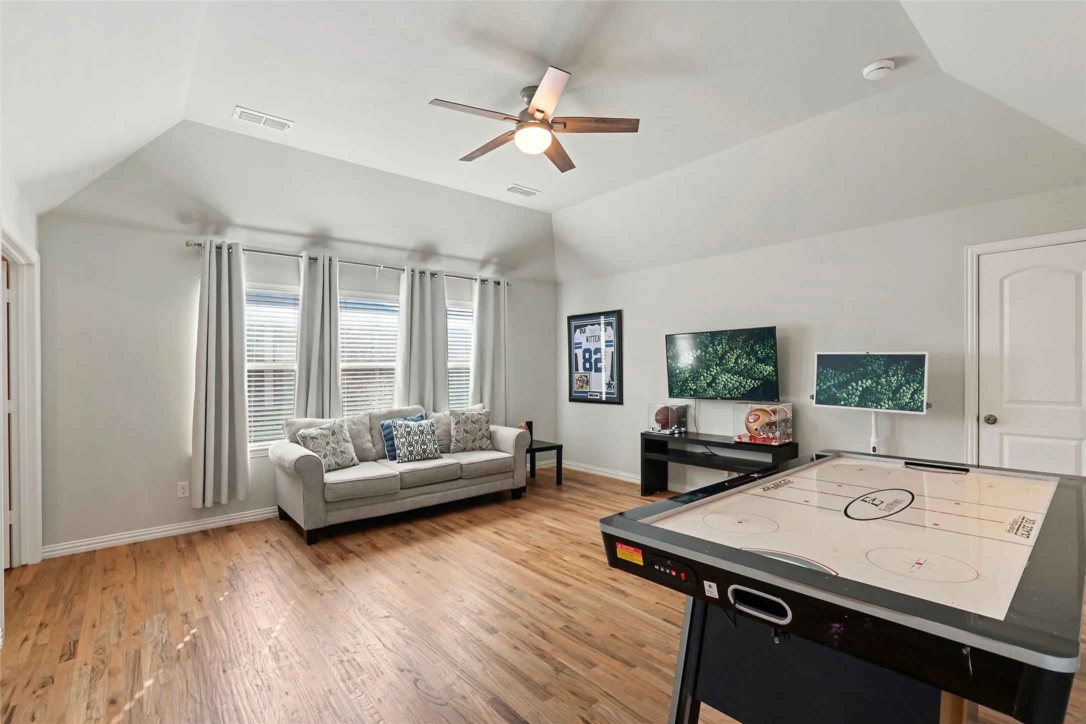 Vaulted ceiling, ceiling fan, wood-finish flooring, multiple windows with blinds, and a white paneled door