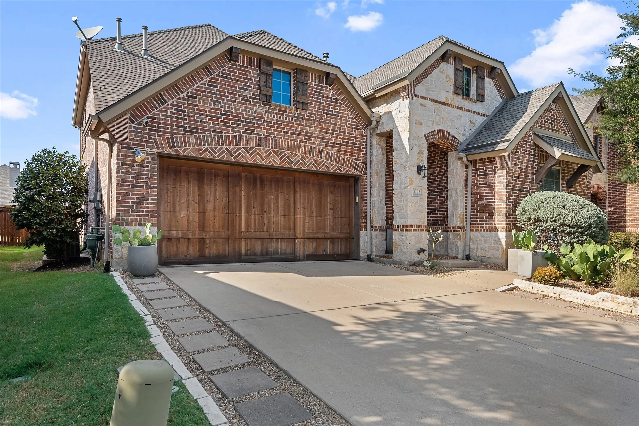 Brick and stone exterior with a wood-finish garage door, gabled roofline, and established landscaping