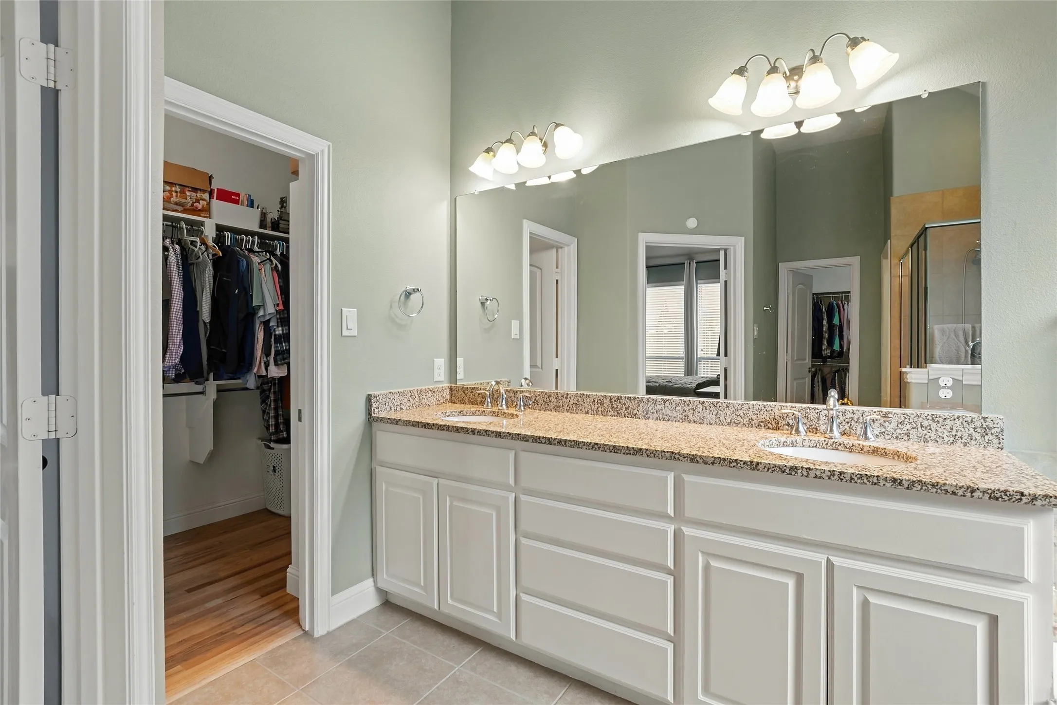 Double vanity with granite countertop, integrated sinks, white cabinetry, and a large mirror