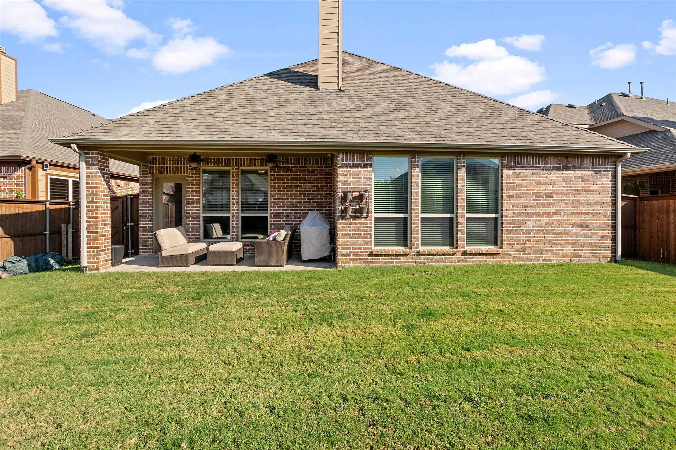 Covered patio with brick columns, multiple large windows, and a shingled roof