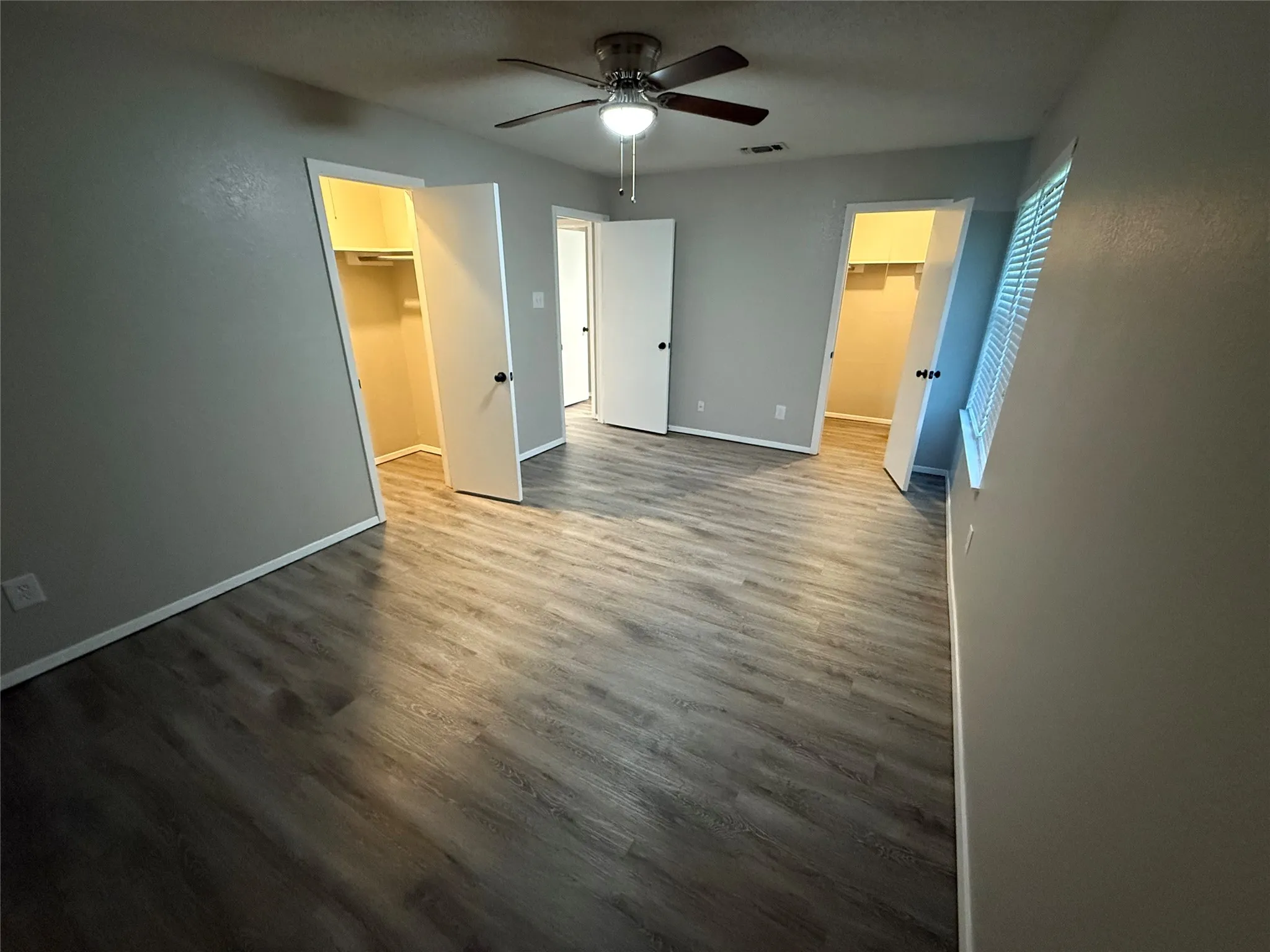 Wood-finish flooring throughout, two open closets with built-in shelving, white trim, and a ceiling fan with integrated lighting