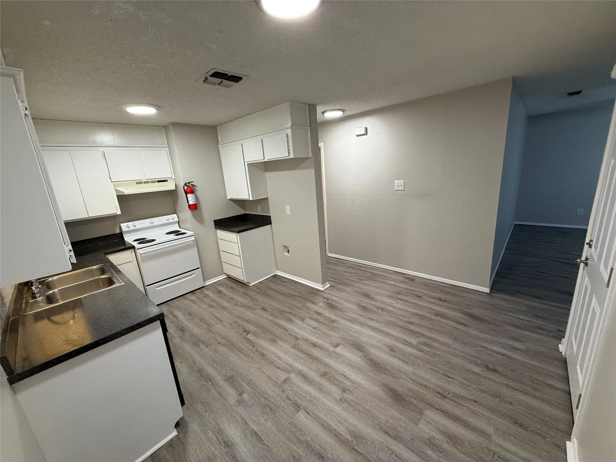 Kitchen featuring white cabinetry, dark countertops, a double basin sink, white range, and wood-finish flooring