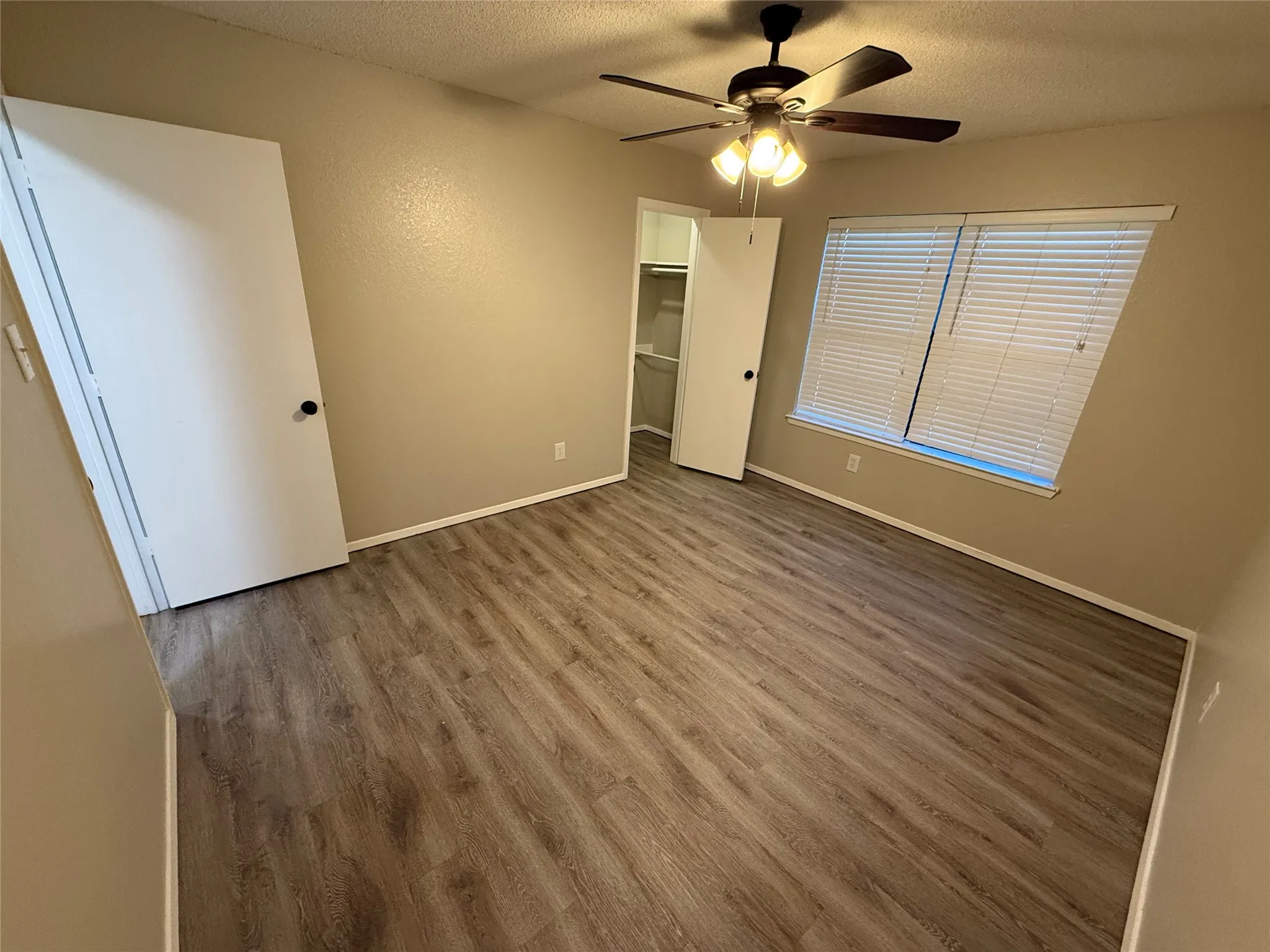 Wood-finish flooring, ceiling fan with integrated lighting, window with blinds, and a built-in closet with shelving