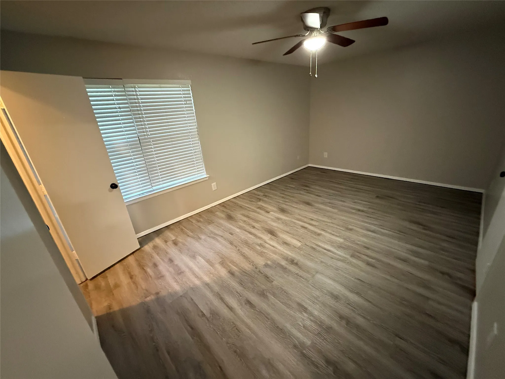 Wood-finish flooring throughout, ceiling fan with integrated lighting, and a window with horizontal blinds