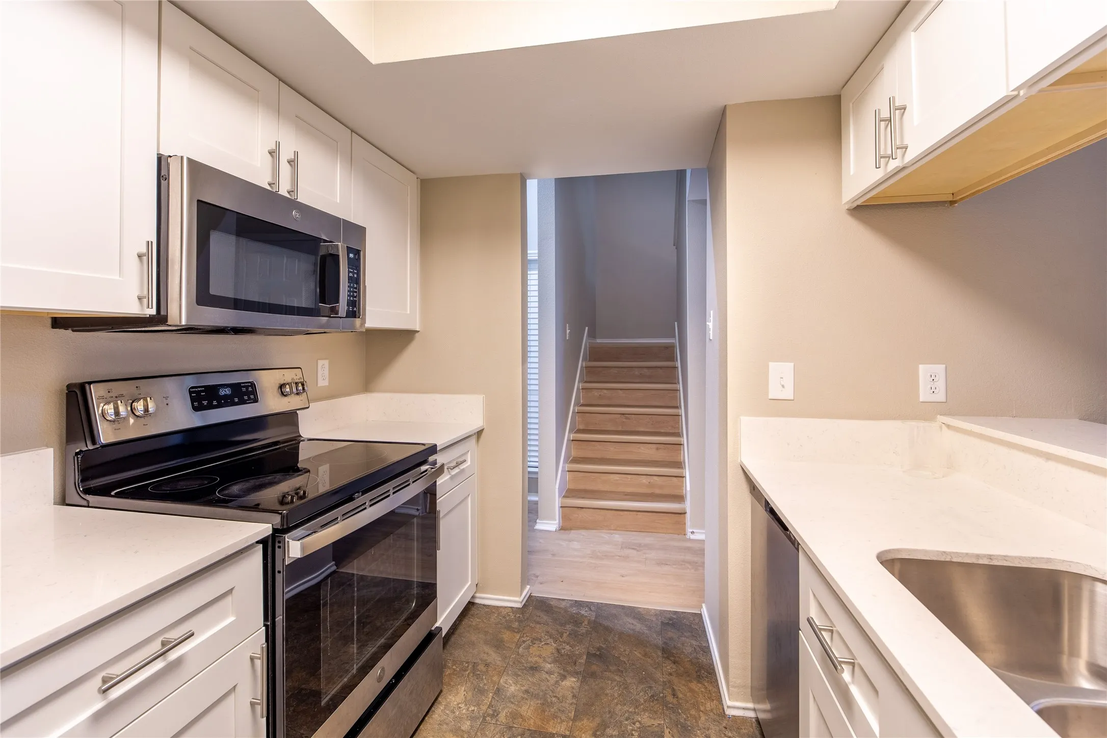 Kitchen featuring white cabinetry, stainless steel appliances, light-colored countertops, and wood-finish flooring on the staircase