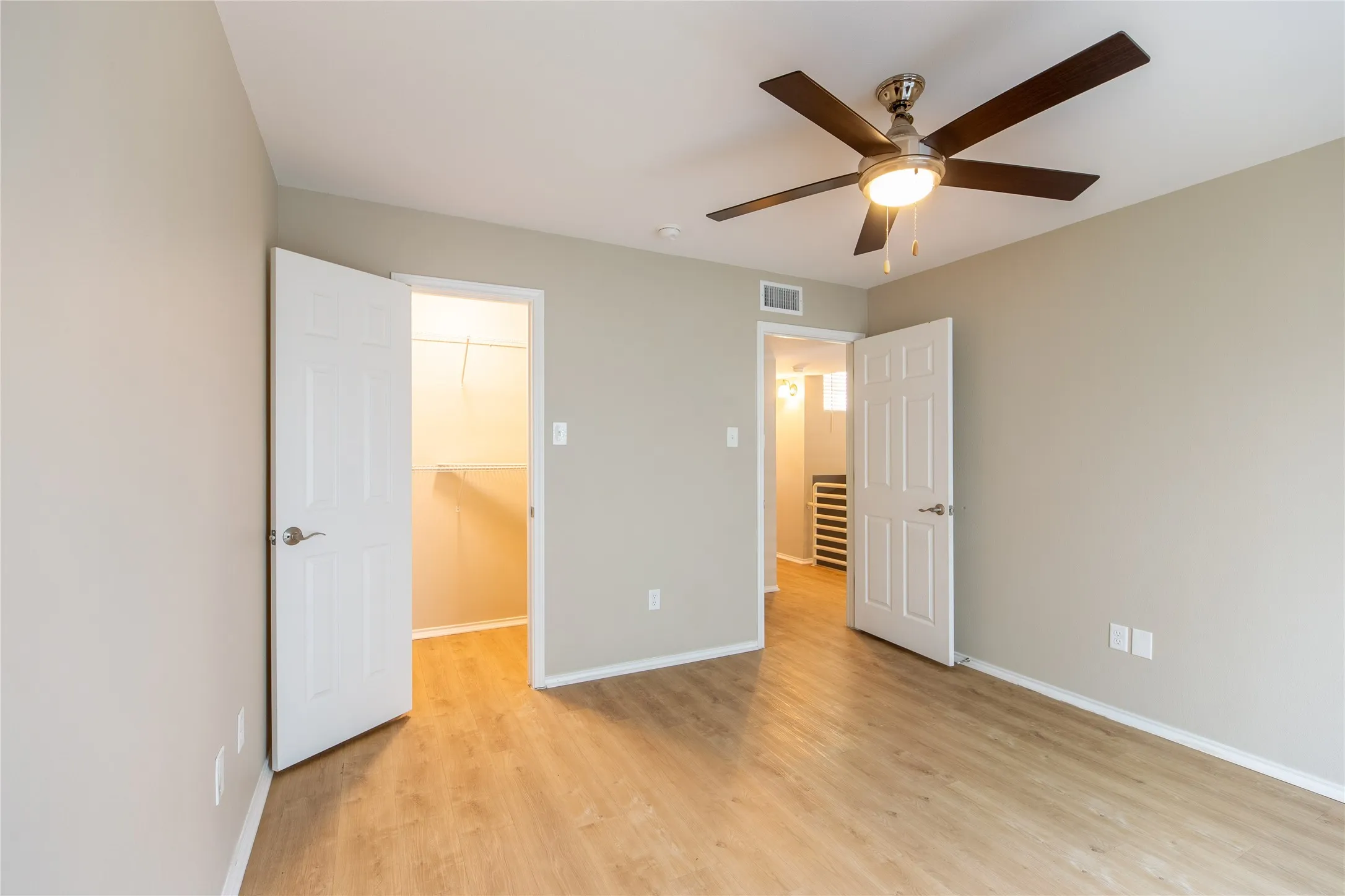 Room with wood-finish flooring, neutral wall tones, a ceiling fan with integrated lighting, and a walk-in closet