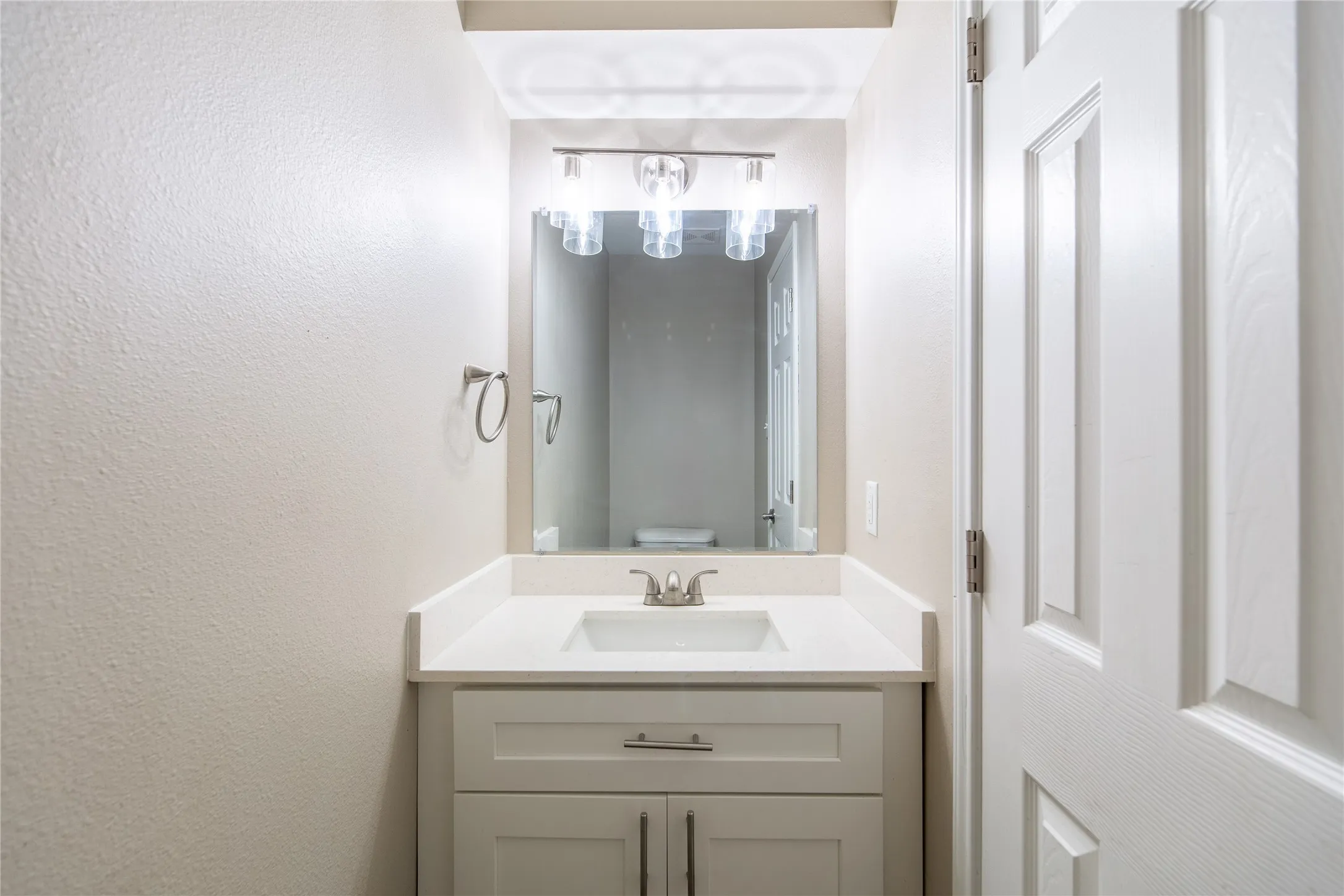 White vanity with brushed nickel hardware, integrated rectangular sink, and light-colored countertop