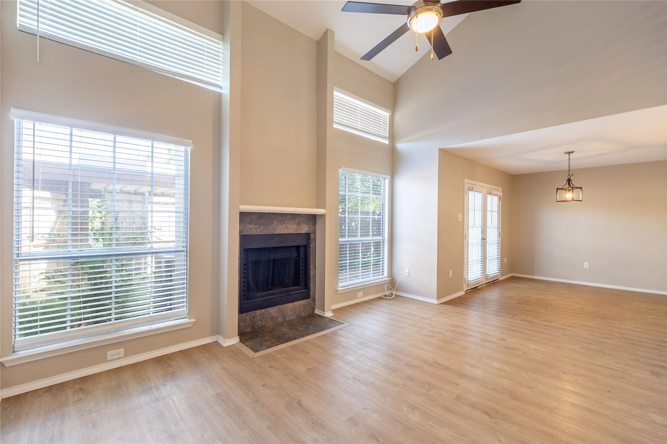 Vaulted ceiling with a ceiling fan, fireplace with a stone surround, wood-finish flooring, two sets of windows, and French doors