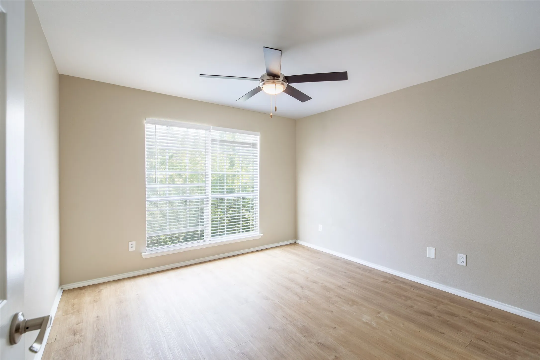 Wood-finish flooring, neutral wall tones, window with horizontal blinds, and a ceiling fan with integrated lighting