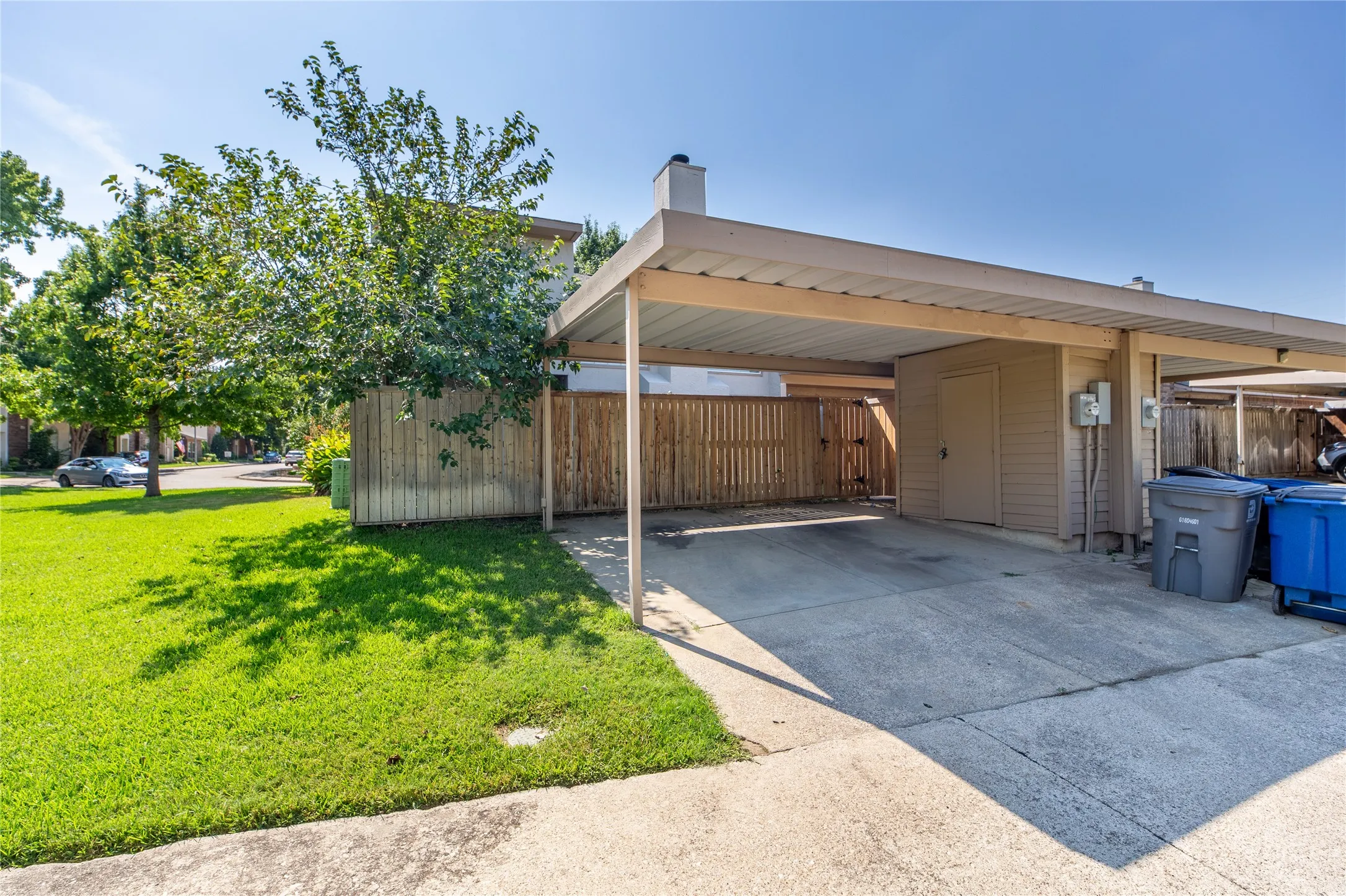 Covered carport parking with an attached storage shed, concrete driveway, and a wooden fence