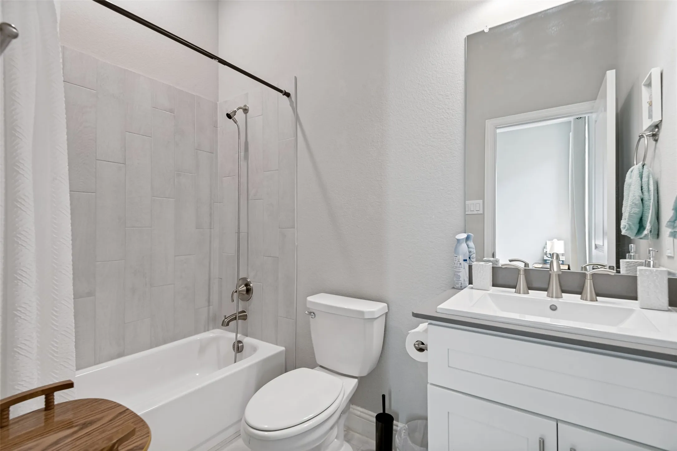 Bathtub with light-colored tile surround, brushed nickel fixtures, white vanity with integrated sink, and a large wall-mounted mirror