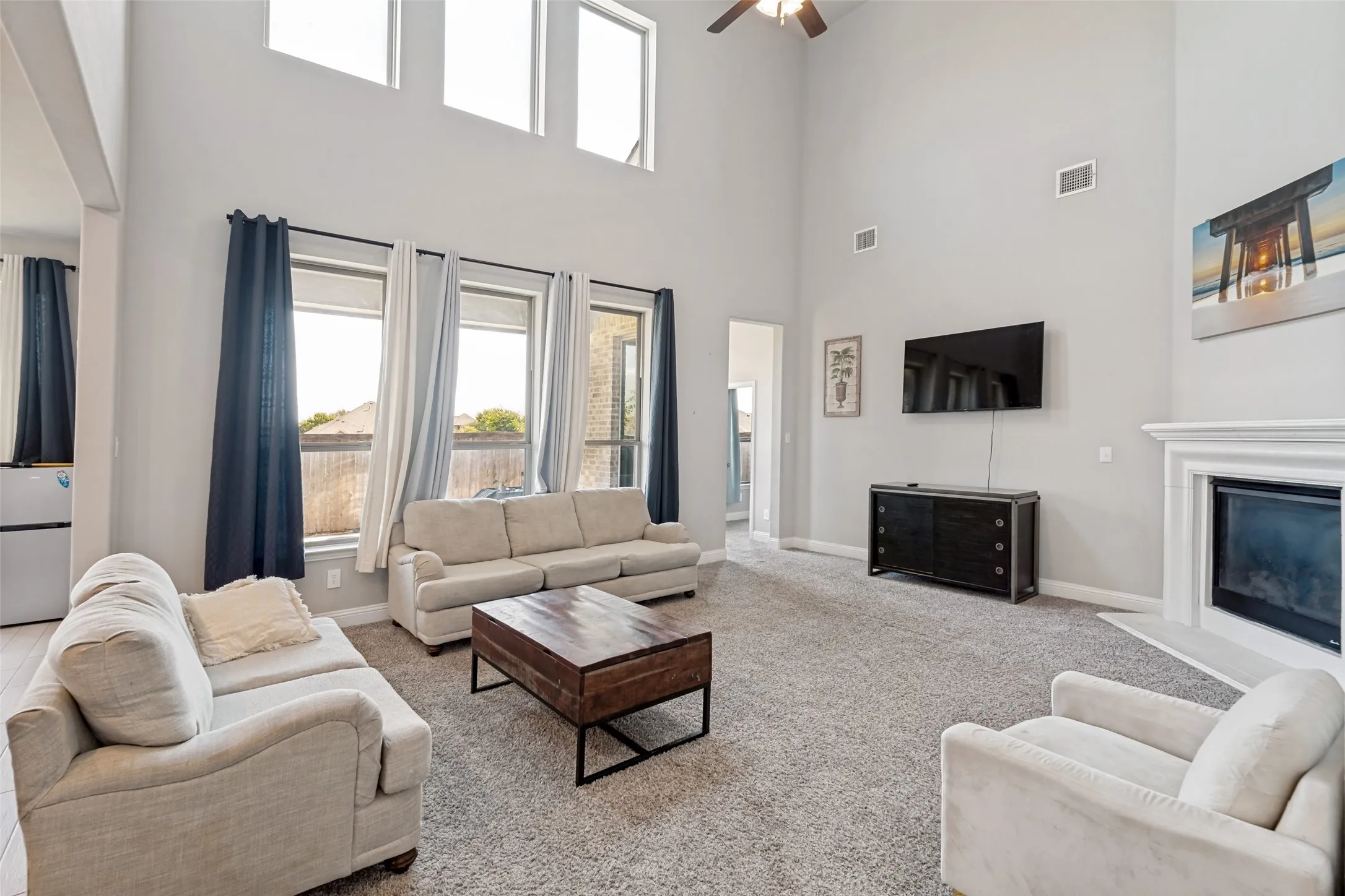 Two-story living area with high ceilings, multiple windows, a ceiling fan, and a built-in fireplace
