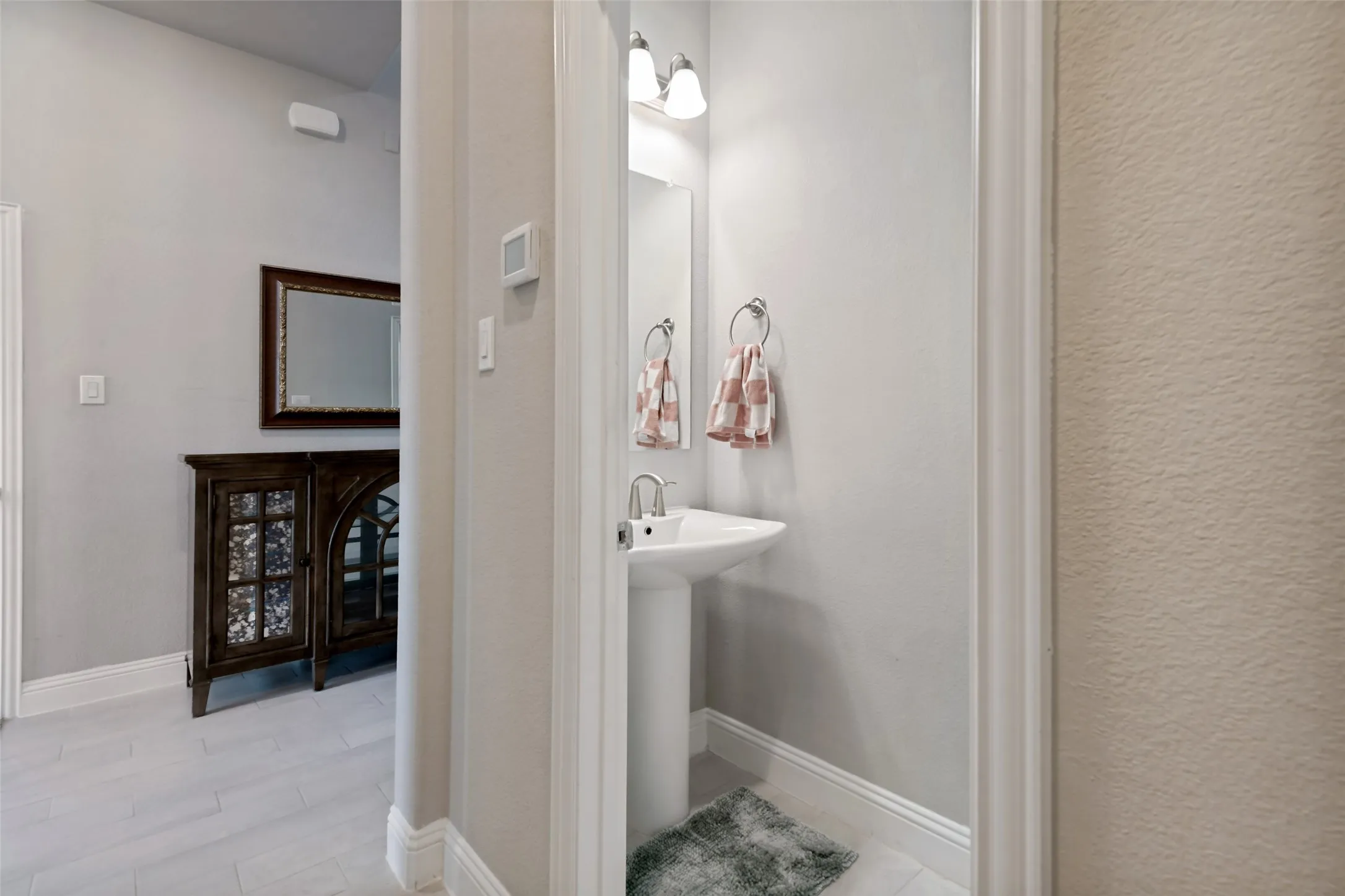 Pedestal sink with chrome faucet, wall-mounted mirror, and overhead vanity lighting