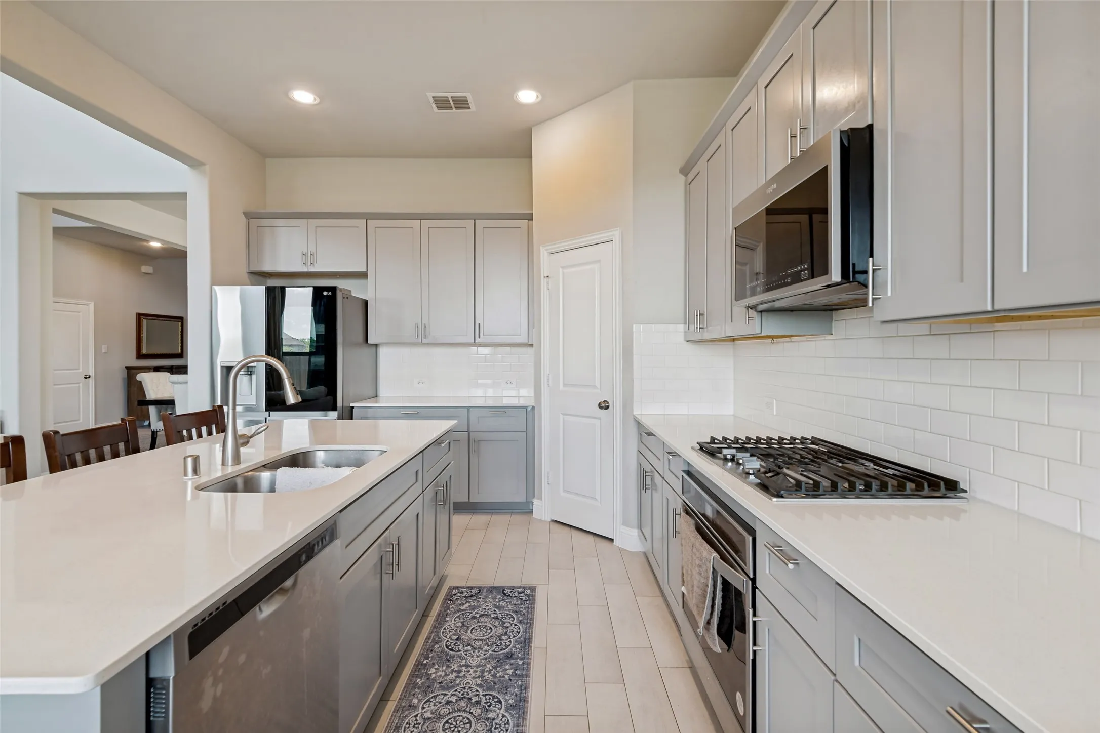 Kitchen featuring a stainless steel sink, gas range, built-in microwave, light gray cabinetry, and white subway tile backsplash