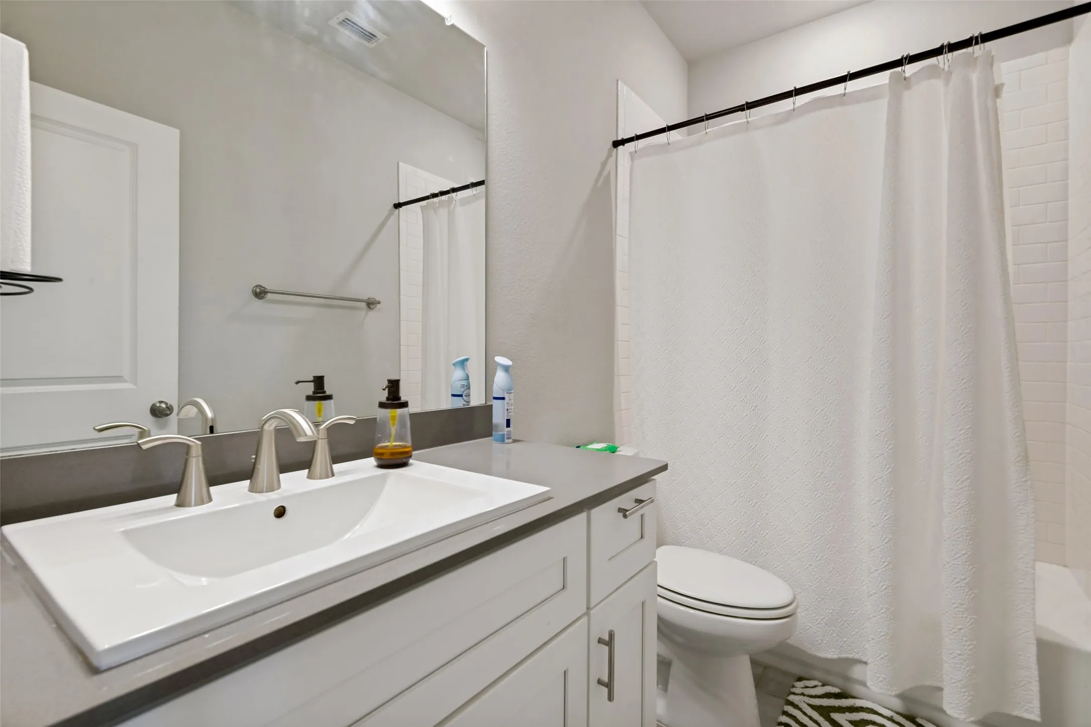 White shaker-style vanity with brushed nickel hardware, light-toned countertop, and undermount rectangular sink with brushed nickel faucet