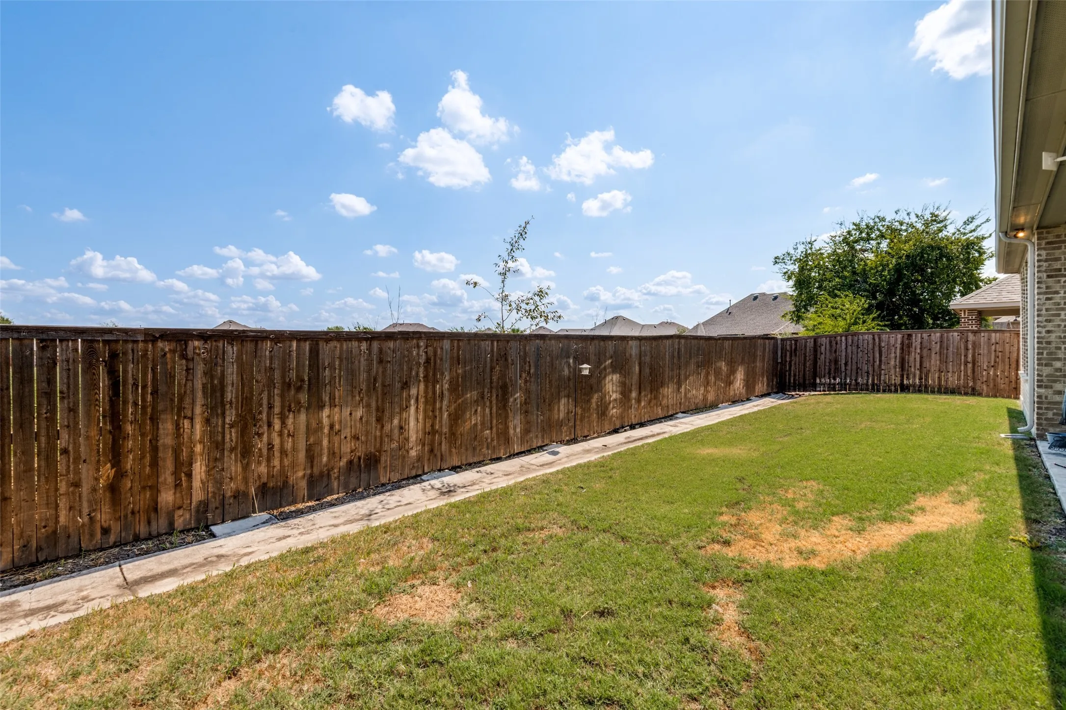 Expansive backyard featuring a wood fence and a brick-finish exterior