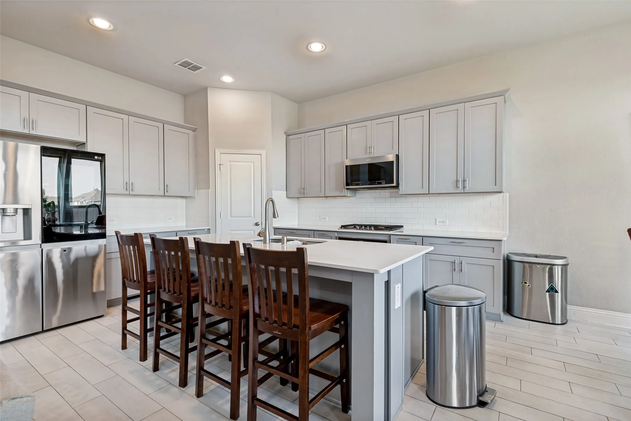 Kitchen featuring light grey cabinetry, white countertops, subway tile backsplash, and stainless steel appliances