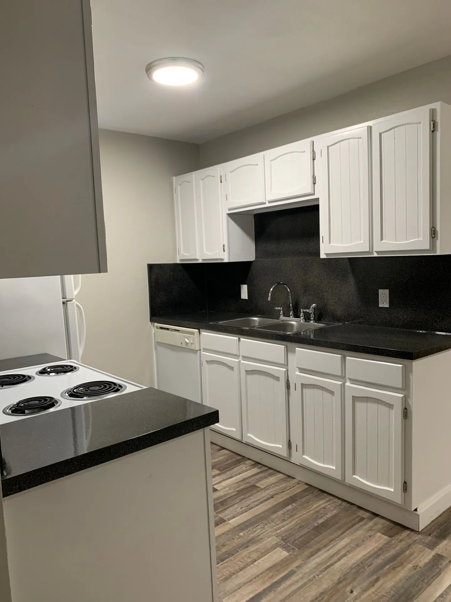Kitchen featuring white cabinetry, black countertops, wood-finish flooring, and a stainless steel sink