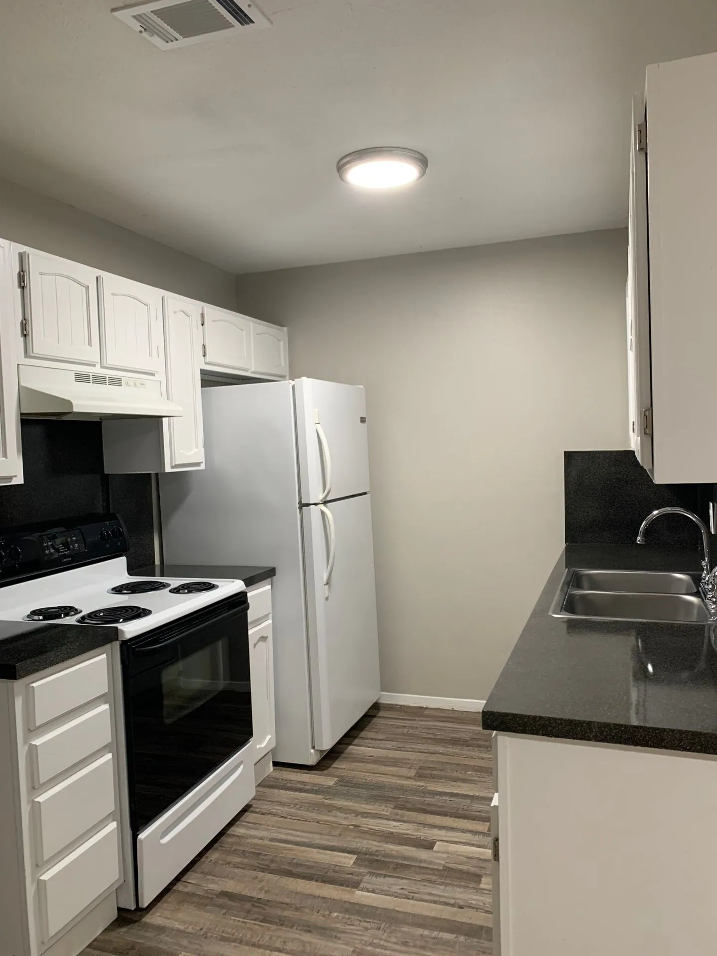 Kitchen featuring white cabinetry, dark countertops, wood-finish flooring, a double basin sink, and a white refrigerator