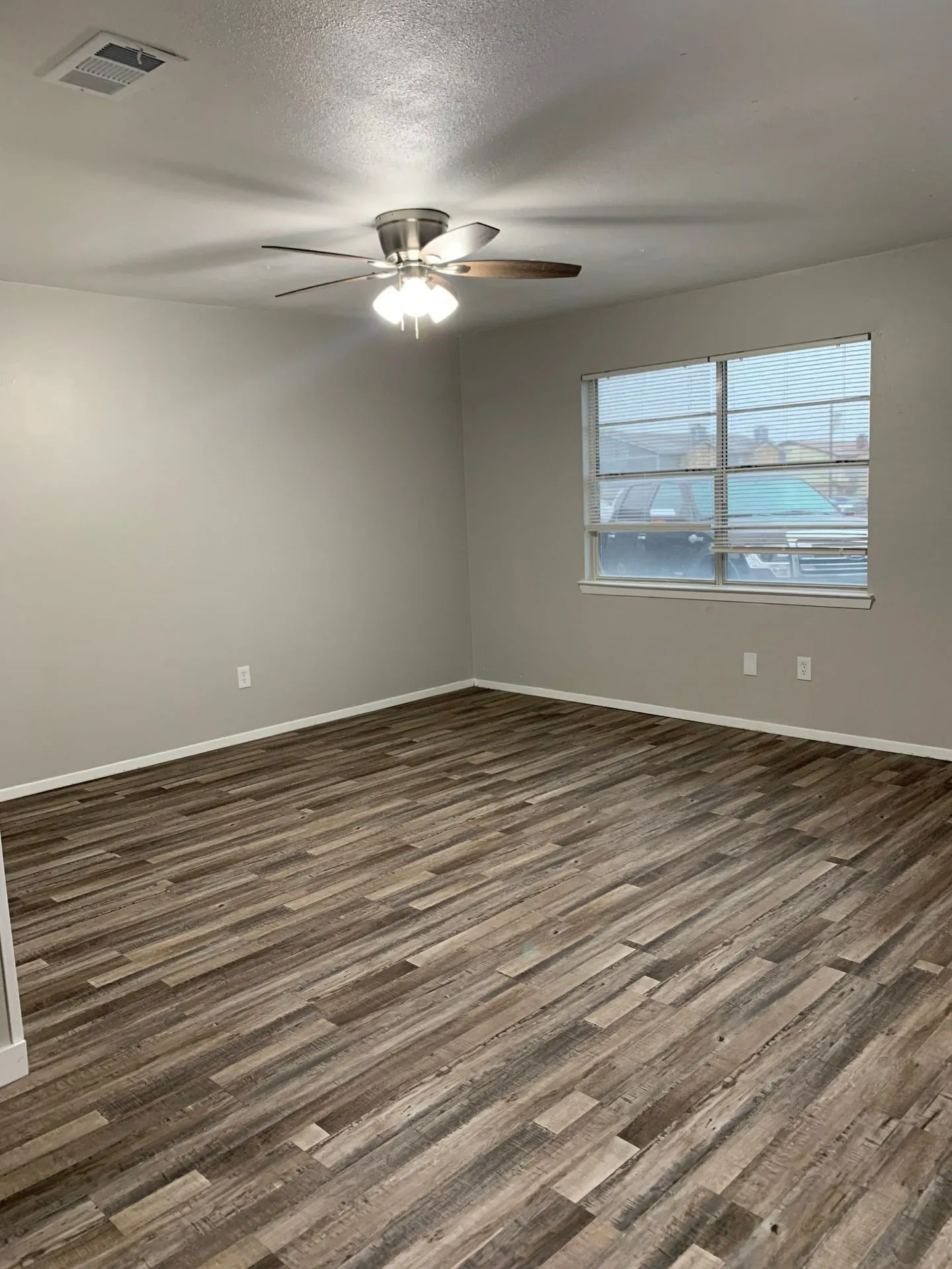 Wood-finish flooring throughout, ceiling fan with integrated lighting, and multiple electrical outlets