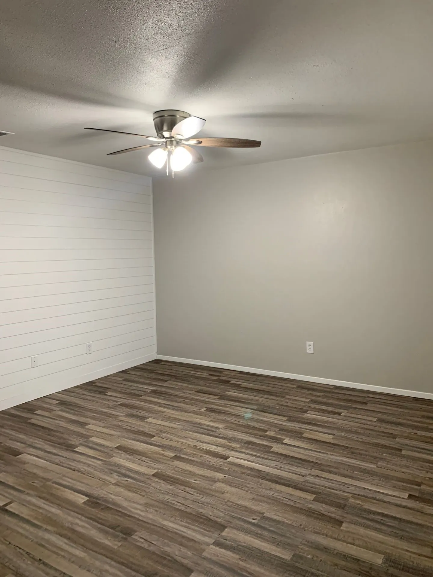 Wood-finish flooring, accent shiplap wall, neutral wall paint, and a ceiling fan with integrated lighting