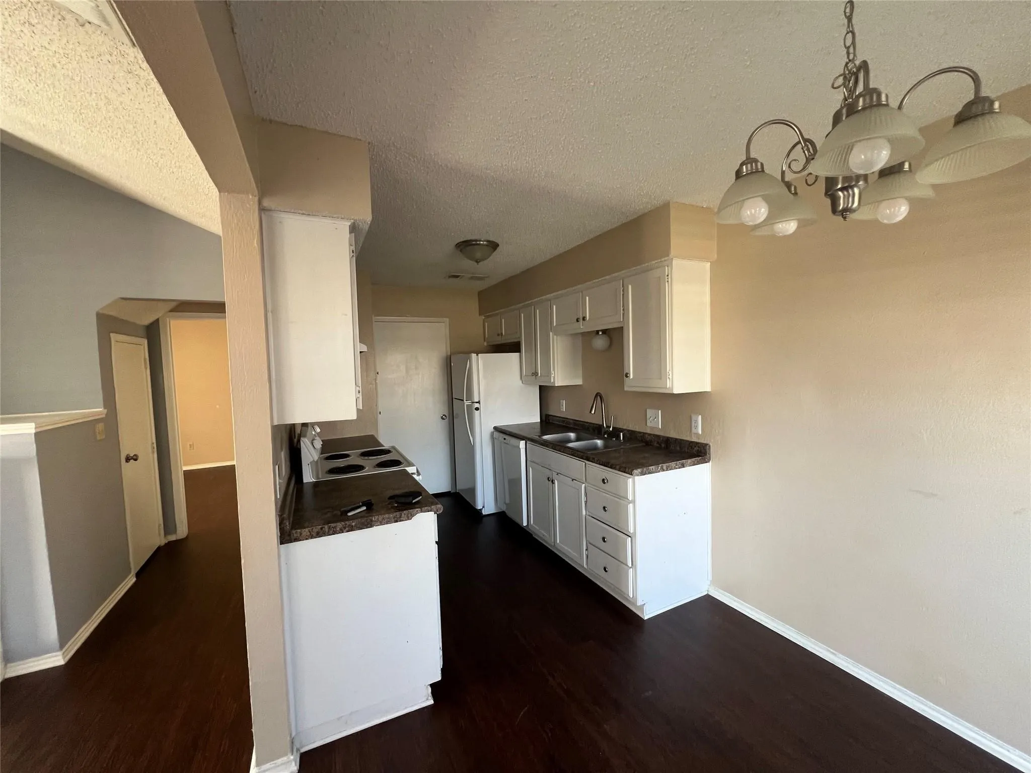 Kitchen featuring dark wood-finish flooring, white cabinetry, dark countertops, and a double basin sink