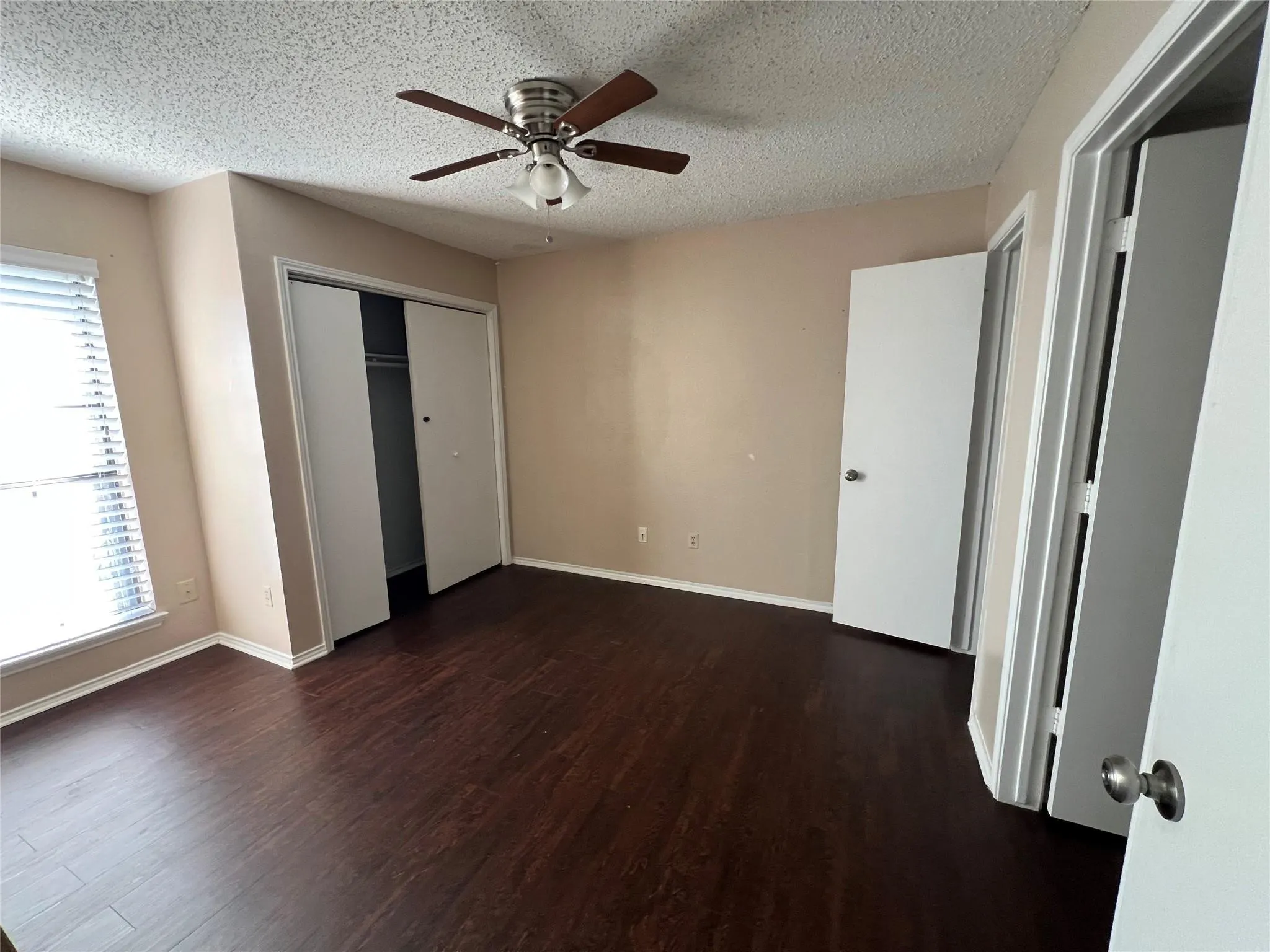 Dark wood-finish flooring, ceiling fan with integrated lighting, dual-panel sliding closet doors, and window with blinds