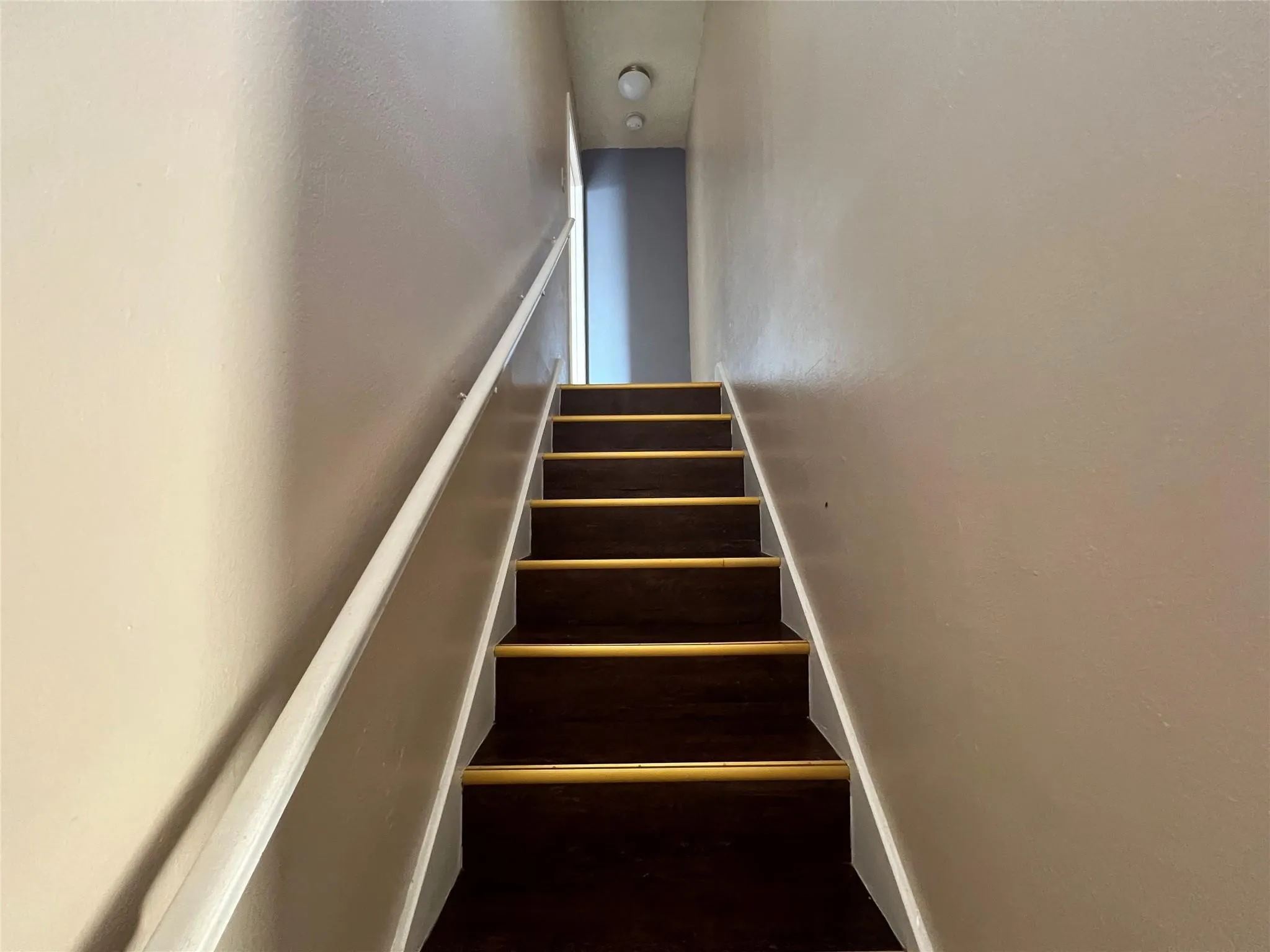 Staircase featuring wood-finish treads and a white handrail
