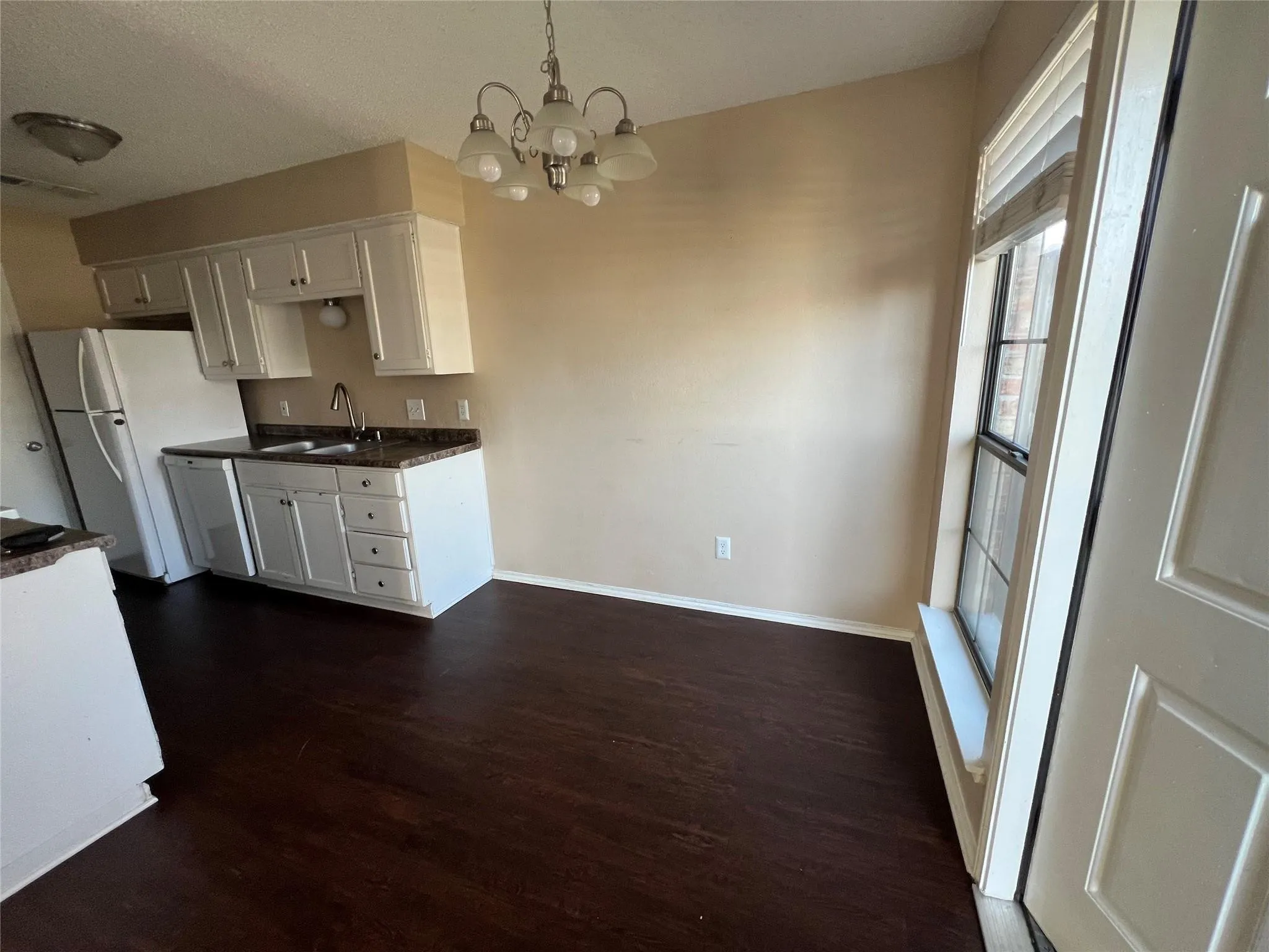 Kitchen with wood-finish flooring, white cabinetry, dark countertops, and a window