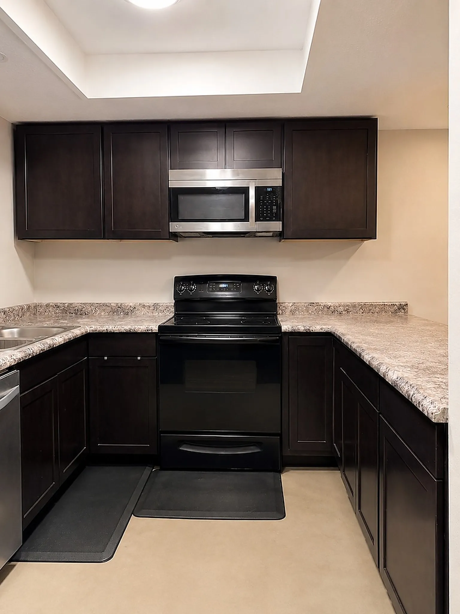 U-shaped kitchen featuring dark wood-finish cabinetry, light-toned countertops, and a full suite of appliances including a black electric range and stainless steel microwave