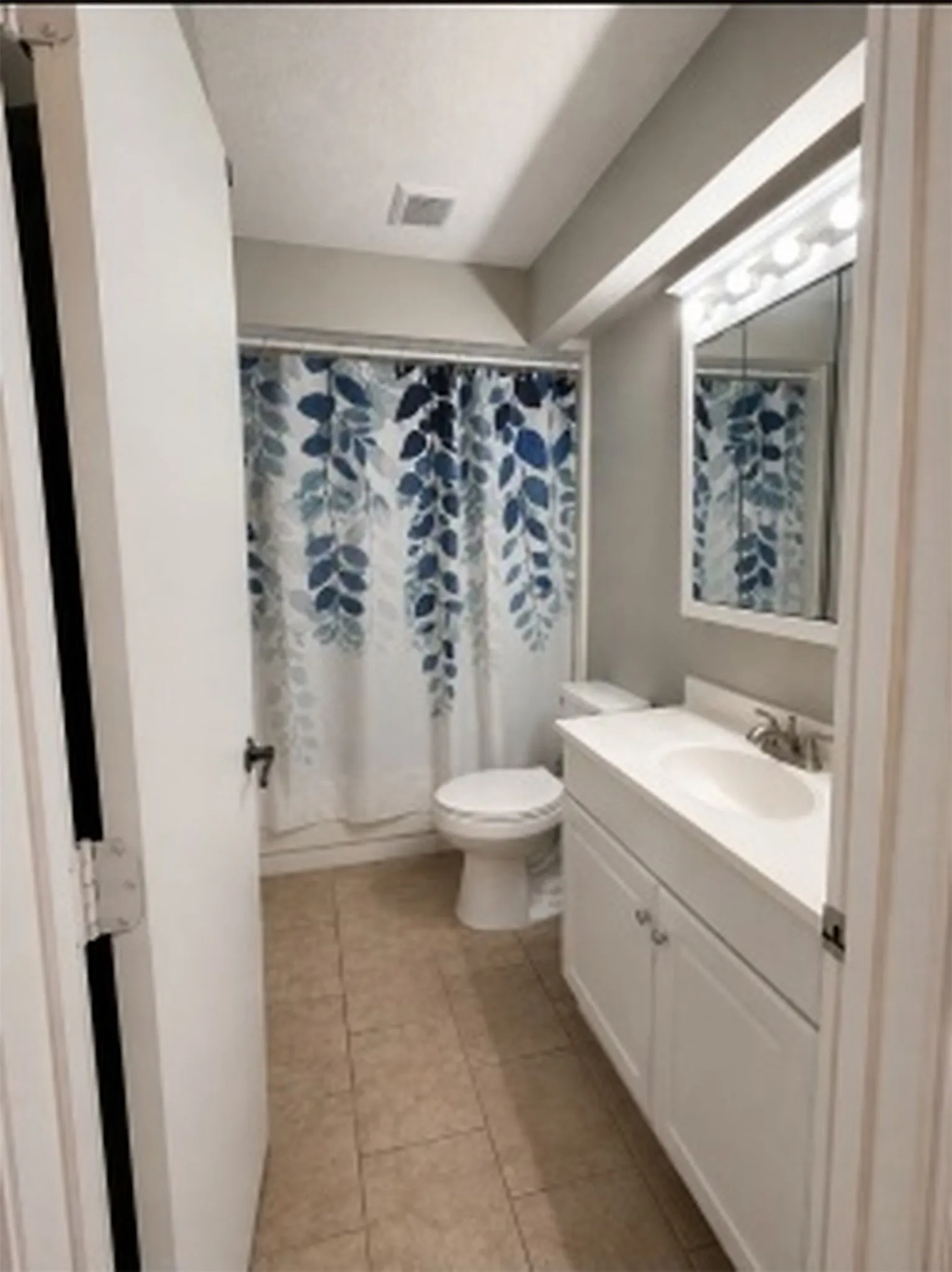 Guest - White vanity with a single basin sink, mounted mirror with vanity lighting, and tile flooring