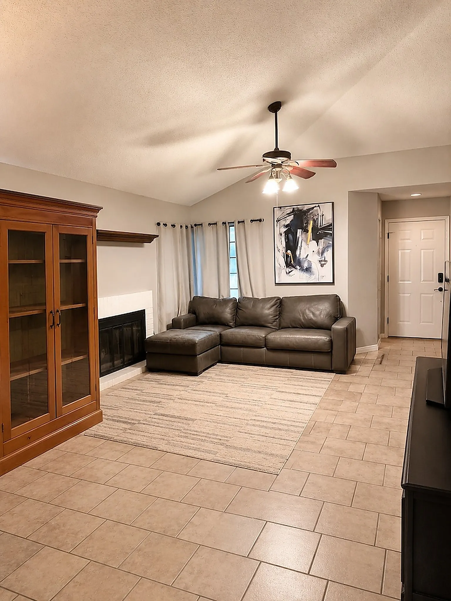 Vaulted ceiling, ceiling fan with lighting, fireplace with mantel, and tile flooring